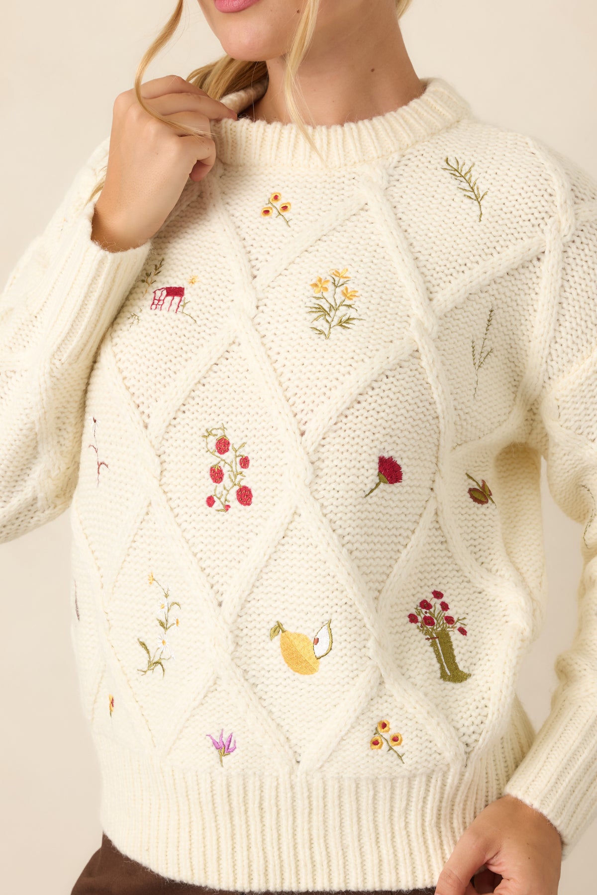 Close-up of the raised diamond knit texture and colorful embroidered flowers, berries, and fruit motifs on the ivory top.