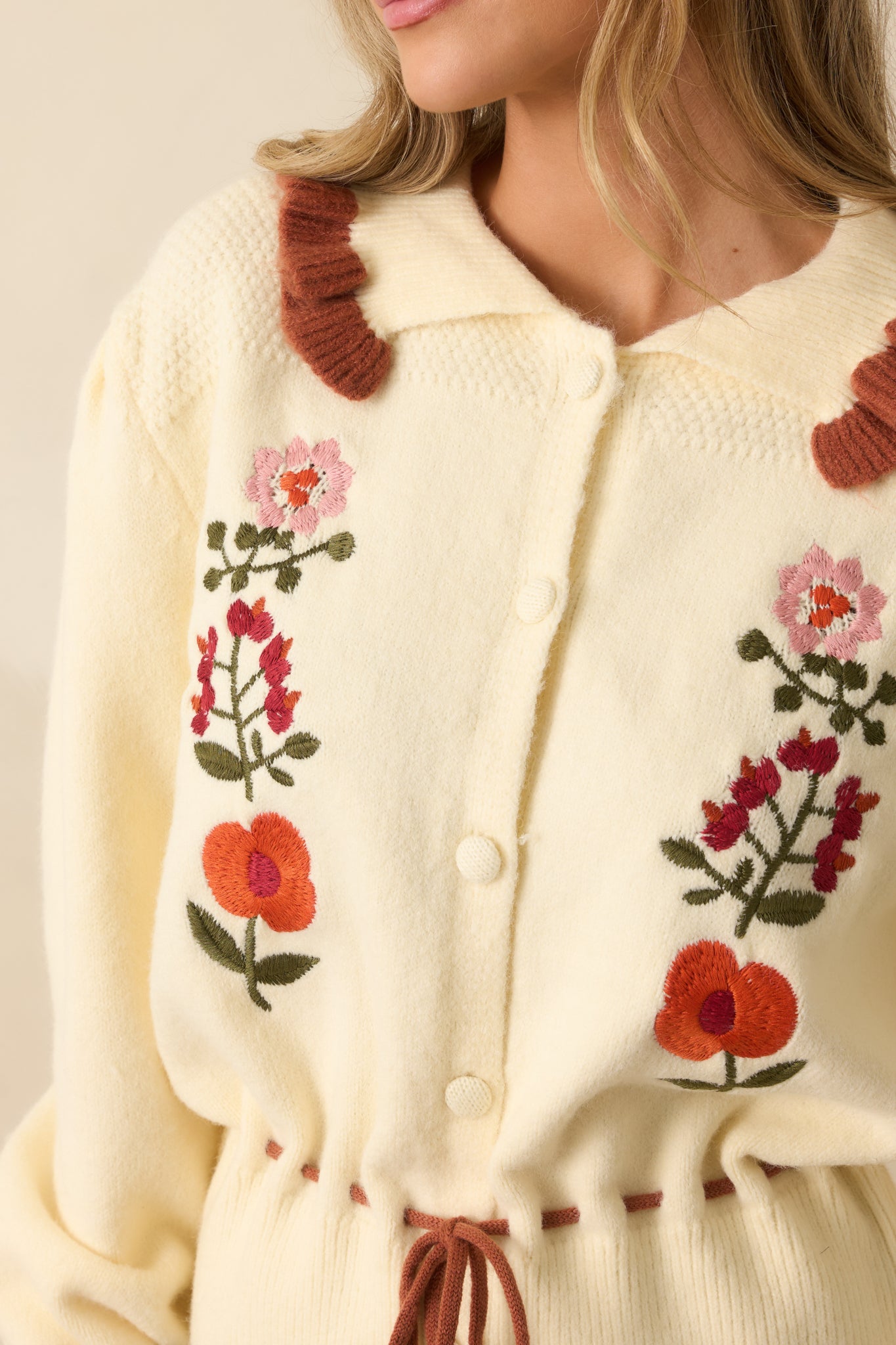 Tight shot of ivory knit fabric showing floral embroidery, rust accents, and ruffle collar.