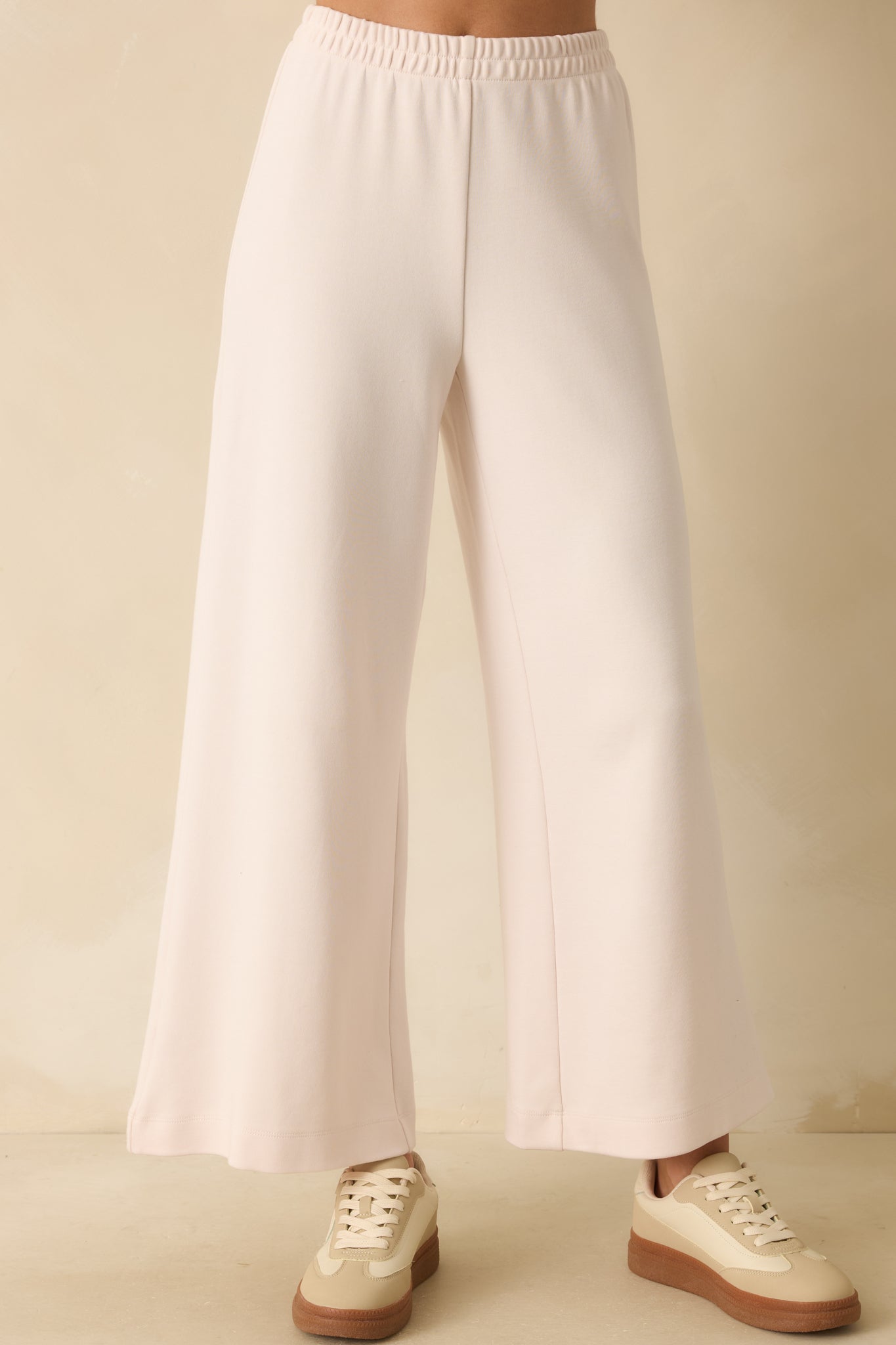Focus on wide-leg silhouette and soft stretch material of ivory knit pants.