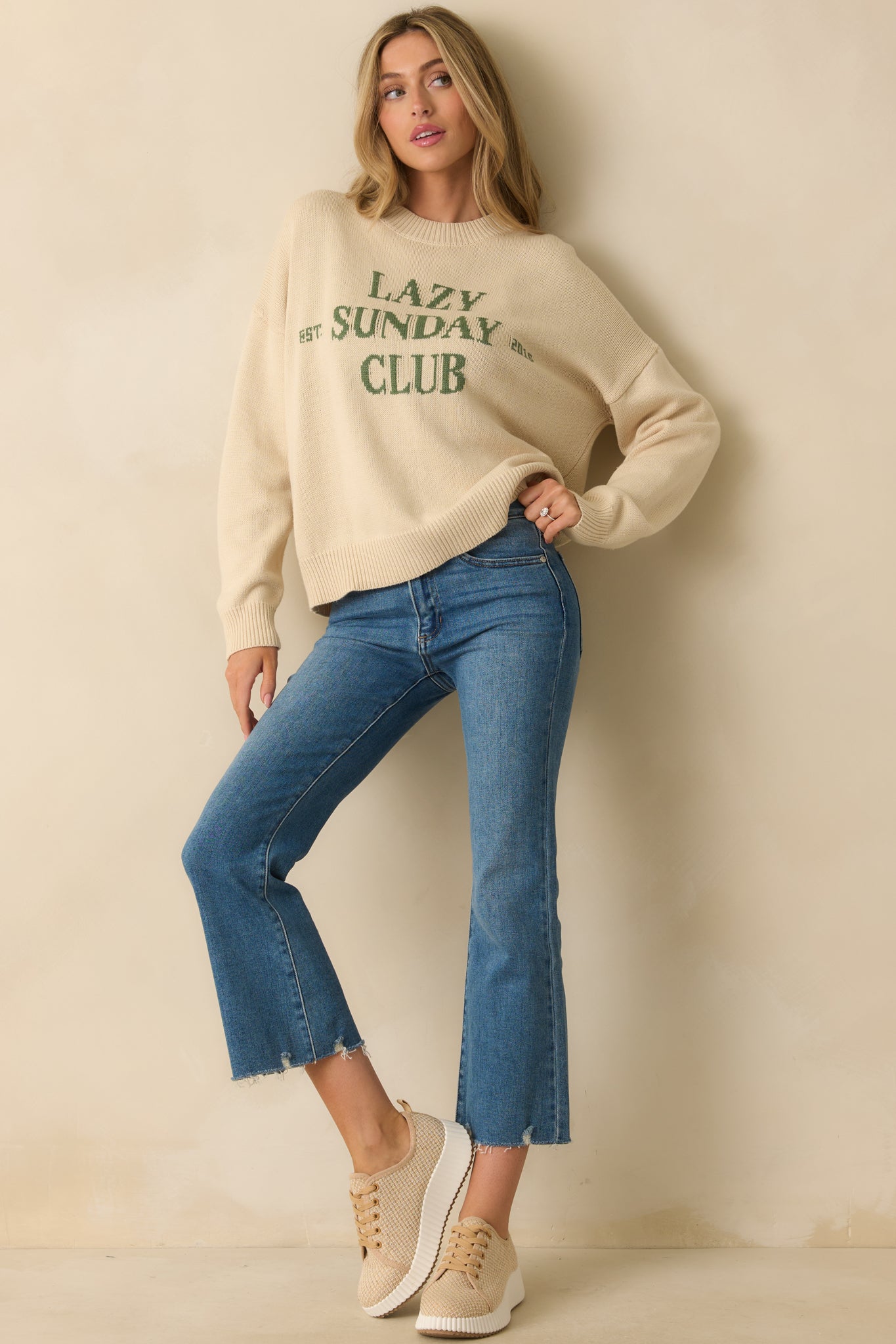 Ivory knit pullover with relaxed fit, drop-shoulder sleeves, and green “LAZY SUNDAY CLUB” graphic across the chest.