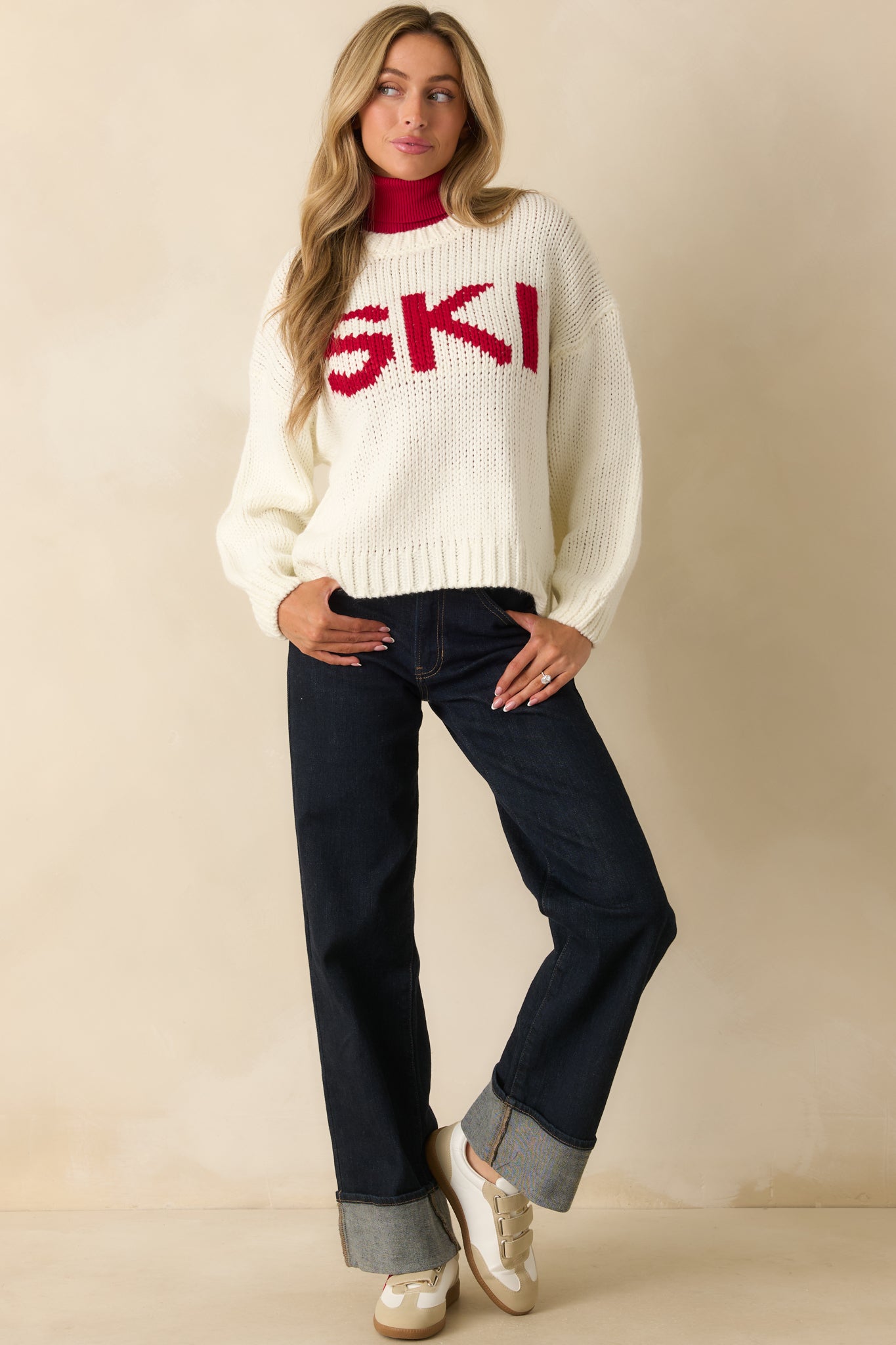 Full-body view of ivory knit sweater with red “SKI” lettering and relaxed fit.