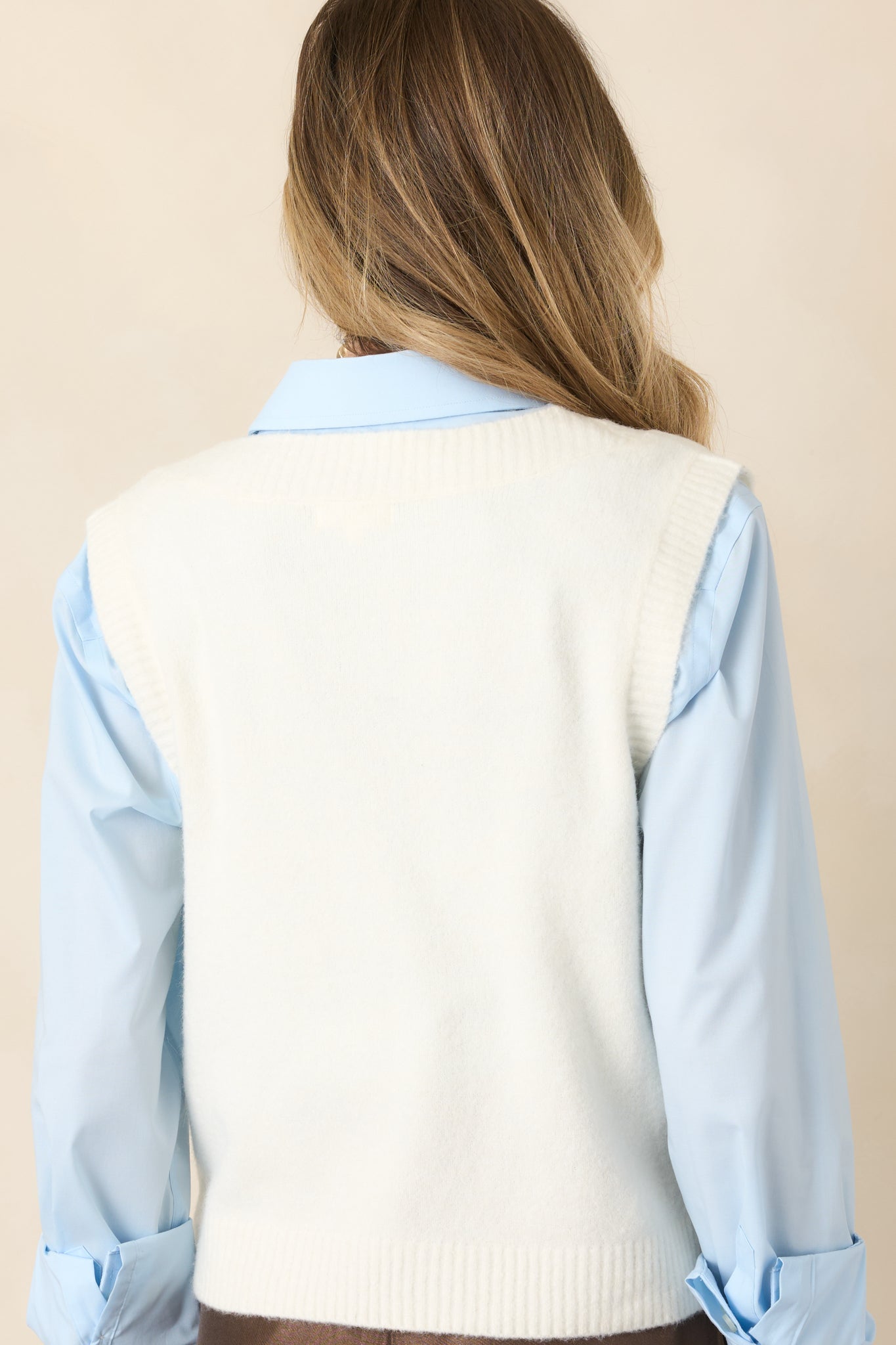 Rear view of the ivory knit vest showcasing its softly textured construction, sleeveless silhouette, and clean ribbed hem.