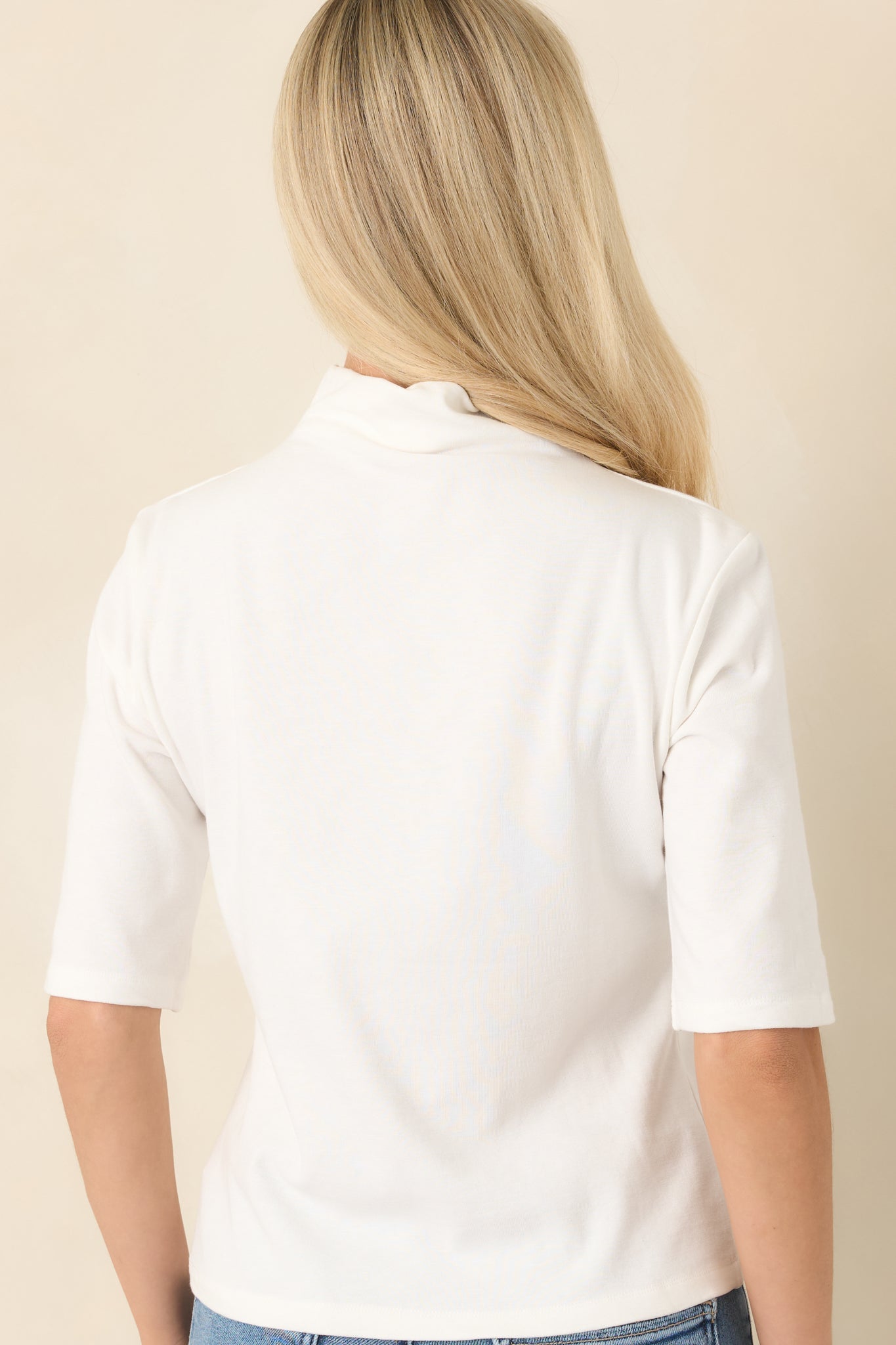 Rear view of the ivory knit top showcasing the smooth back, softly fitted silhouette, elbow-length sleeves, and clean construction for a polished finish.