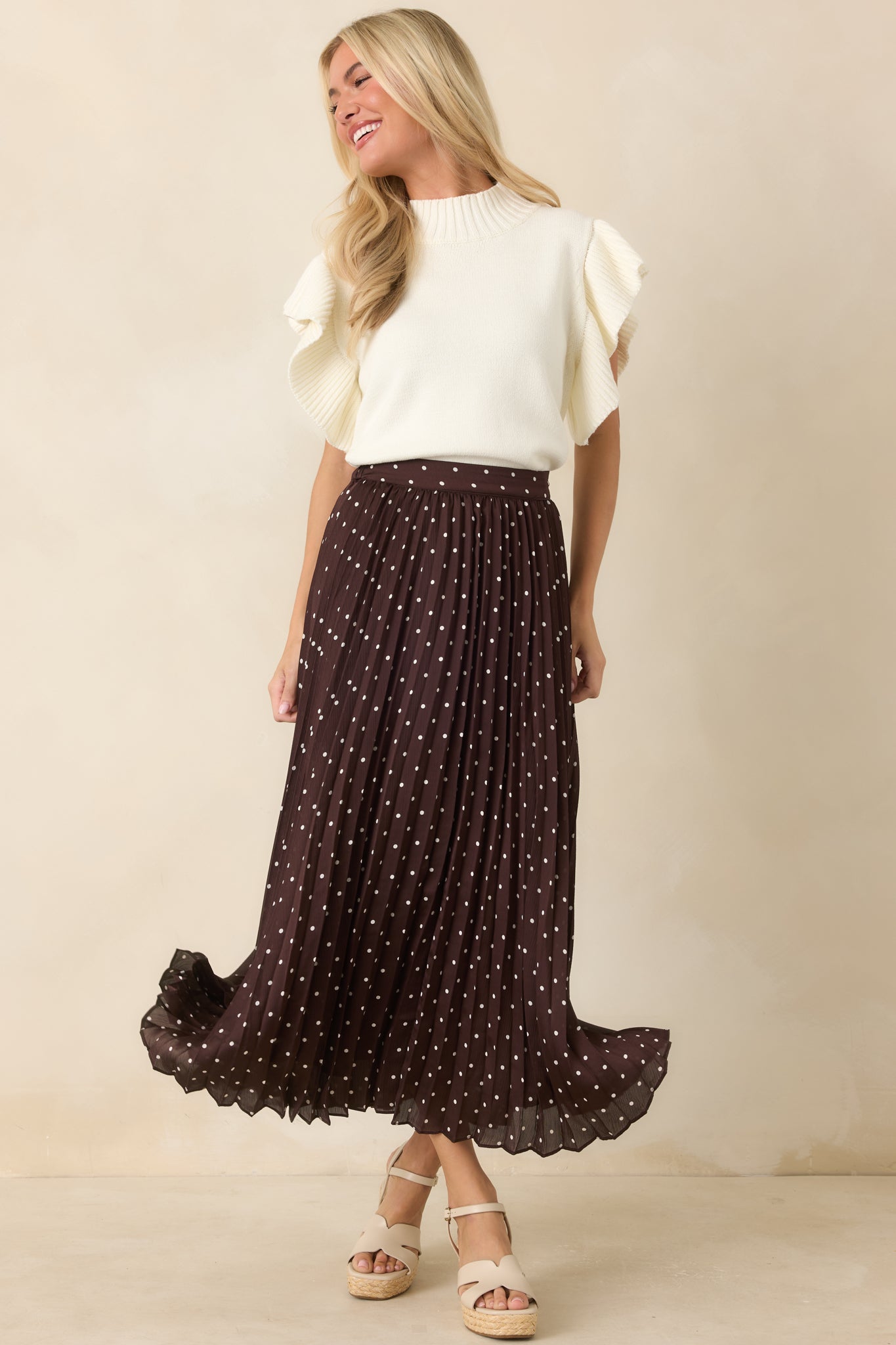 Ivory knit top featuring dramatic ribbed flutter sleeves, mock neckline, and textured hem detail.