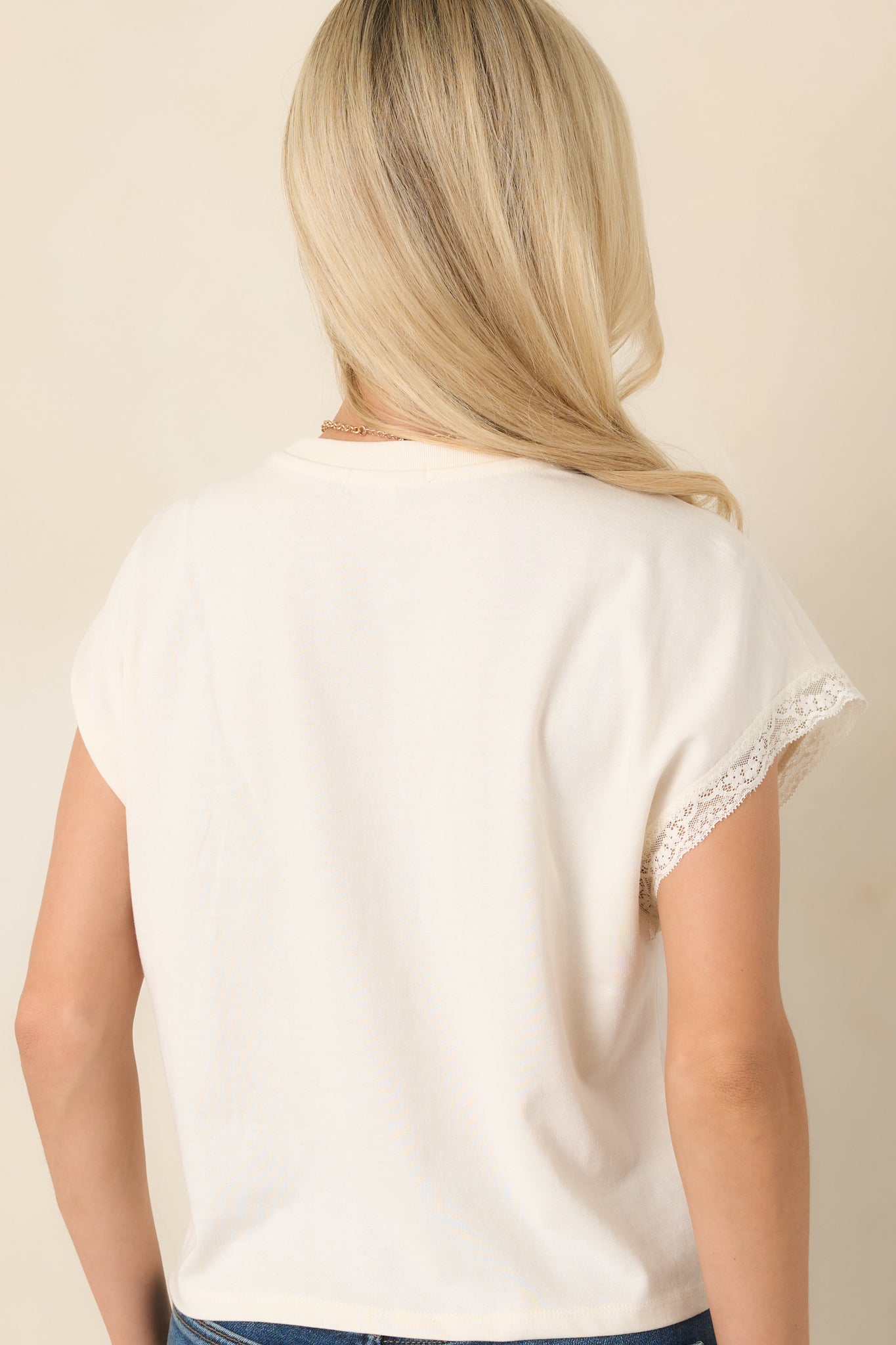 Rear view of the ivory cotton-lyocell top showing its relaxed fit, lace-trimmed cap sleeves, crew neckline, and slightly cropped hem.