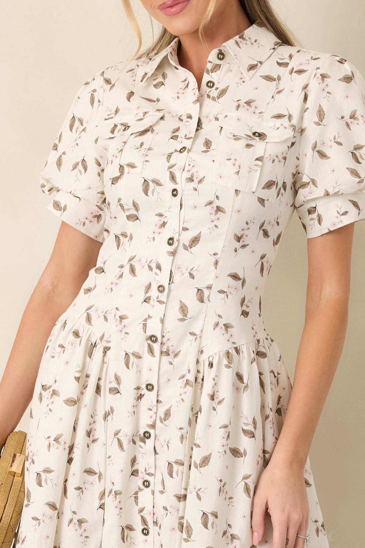 Close-up highlights the ivory linen-blend fabric, delicate floral print, pointed collar, button front, and puff sleeve details.