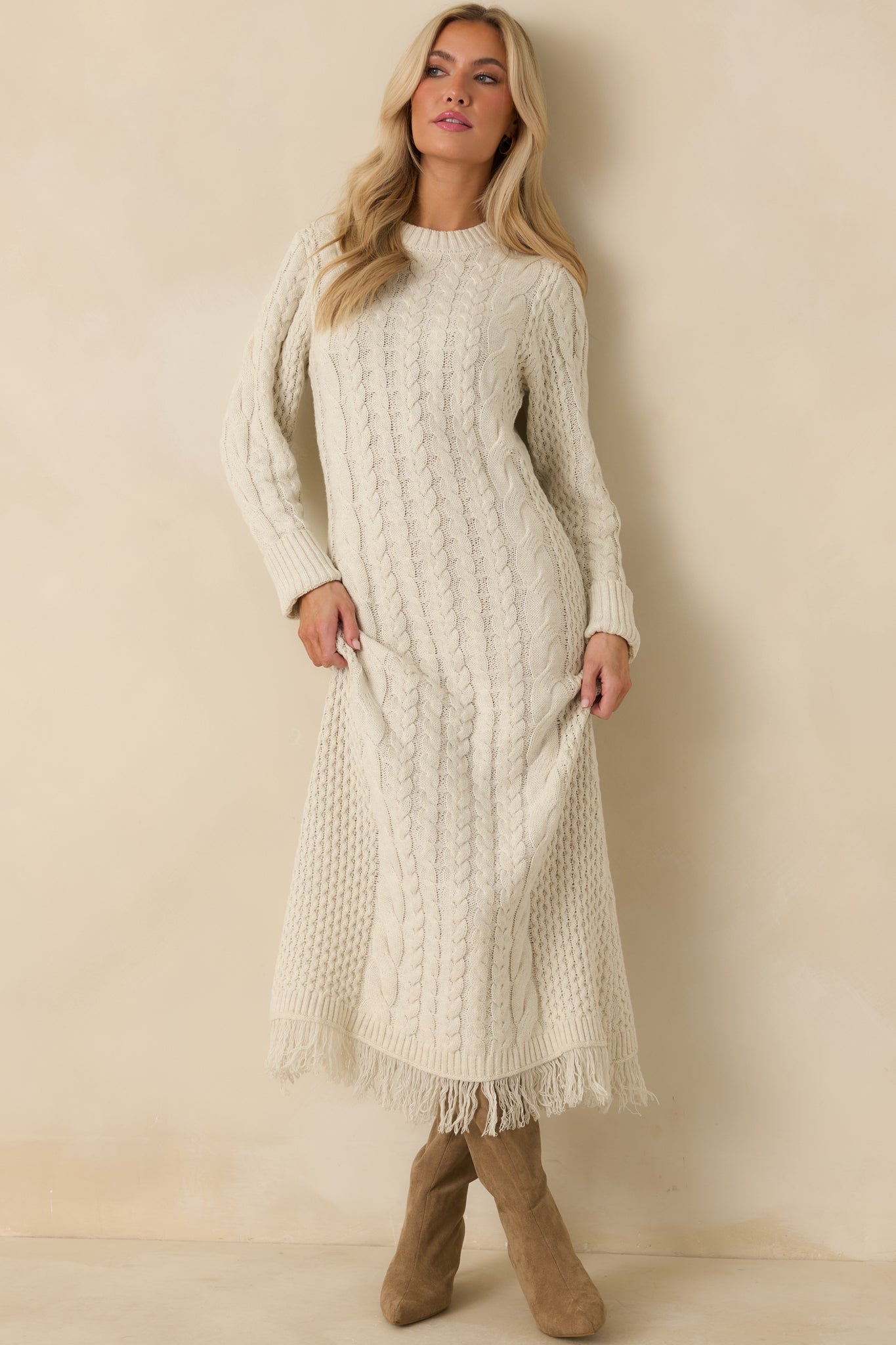 Long sleeve ivory sweater dress featuring mixed cable textures, a relaxed column silhouette, and fringe trim.