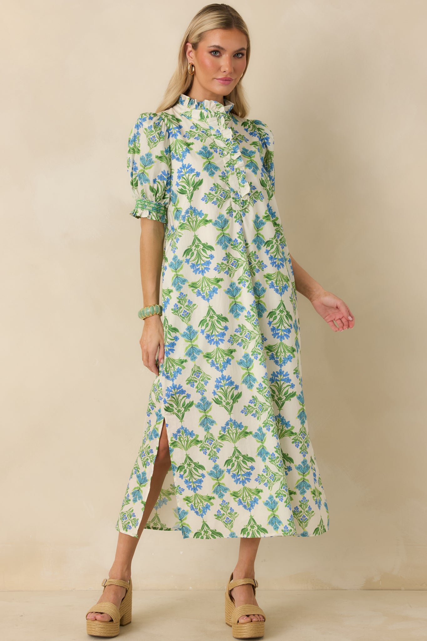 Ivory maxi dress with blue and green floral print, featuring a ruffle-trimmed neckline and short puff sleeves with elastic cuffs.