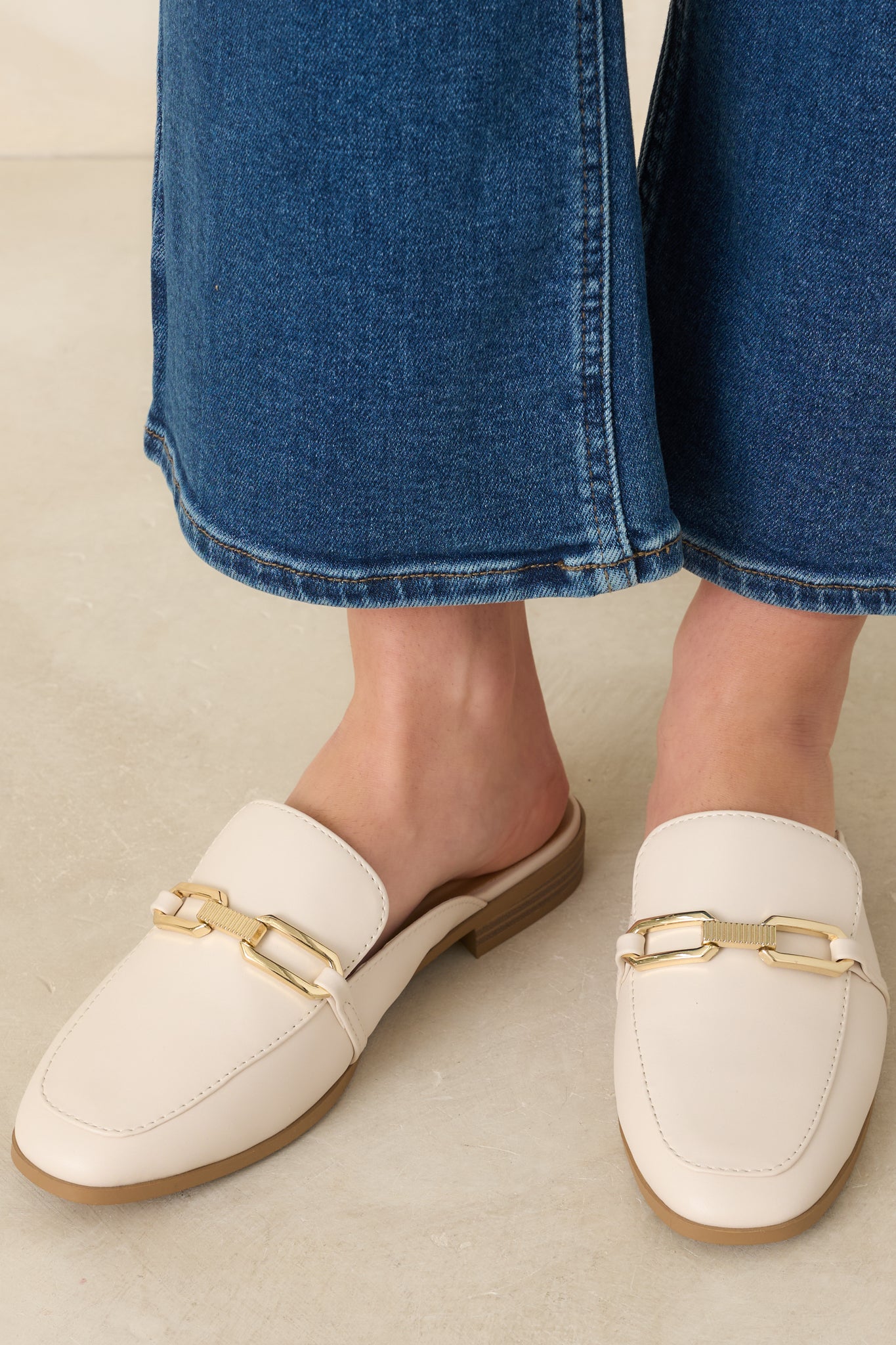 Close-up of ivory mule loafers showing almond toe, polished gold hardware, and lightly cushioned footbed.