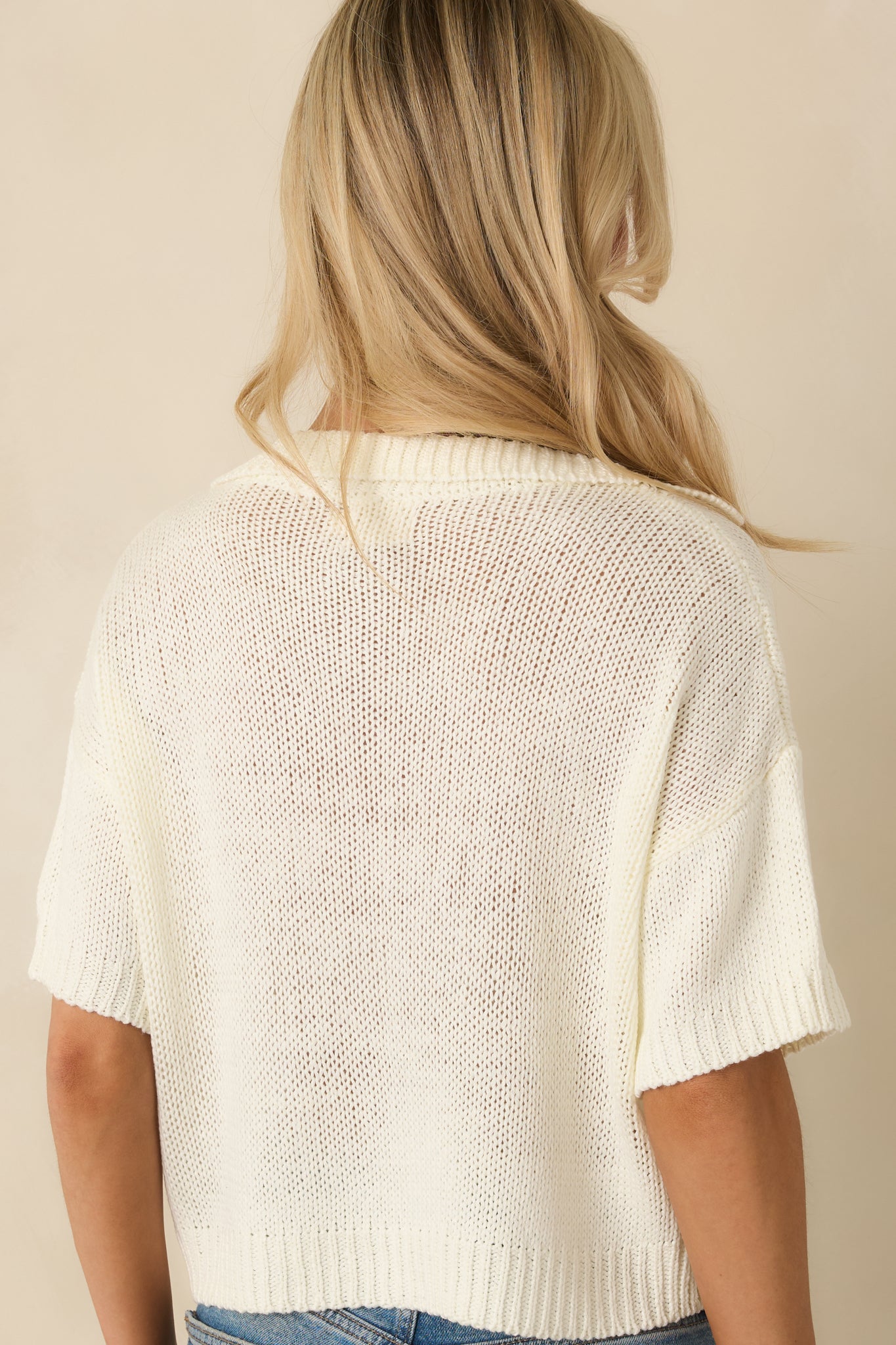 Ivory open-knit sweater showing the rear with a clean knit finish, ribbed hem, and short sleeves beneath the collar.