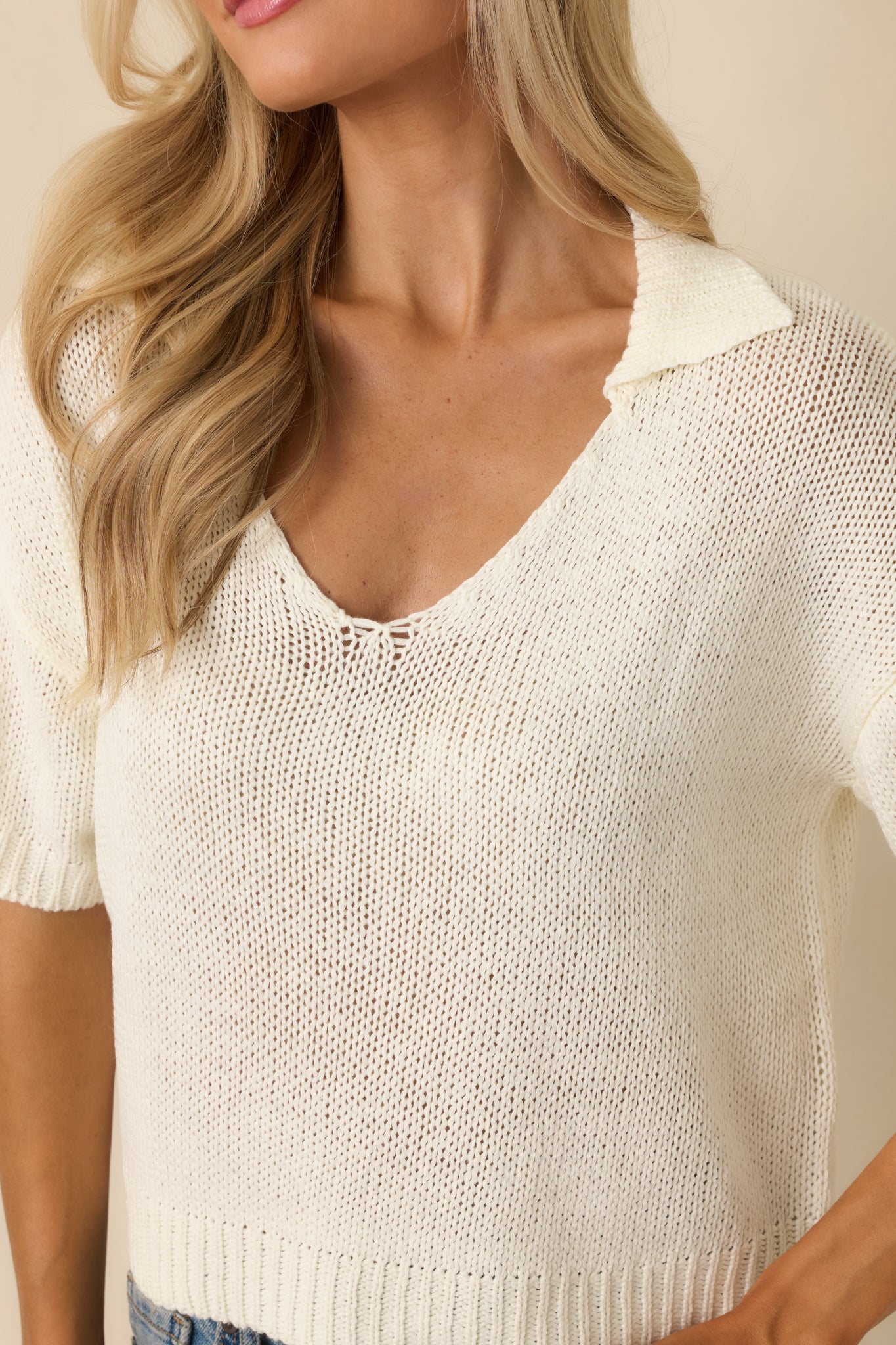 Detailed look at the ivory open-knit fabric highlighting the breathable knit texture, ribbed hem, and collared V-neckline.