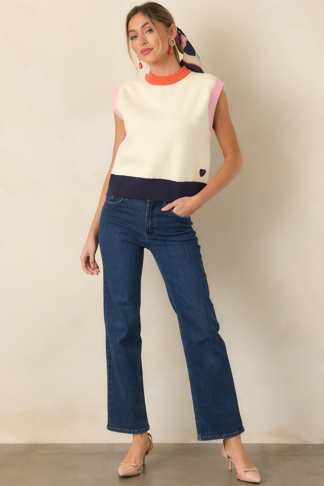 Color-blocked sleeveless top featuring an ivory body framed by an orange neckline, pink-trimmed armholes, and a contrasting navy ribbed hem.