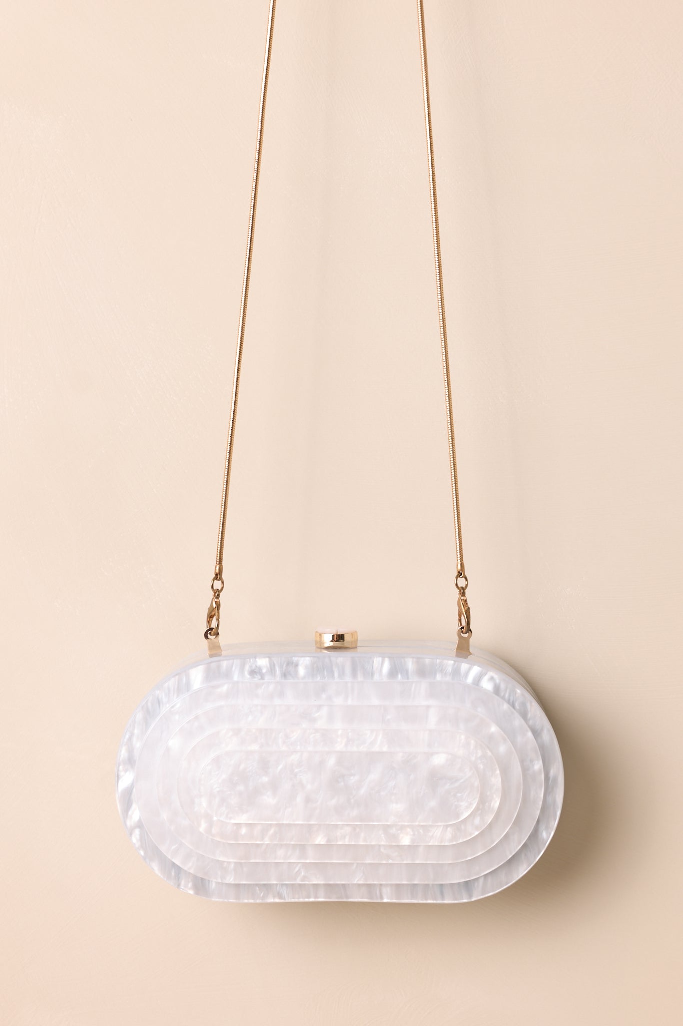 A full view of the ivory oval clutch with a pearlescent finish, layered front design, and gold tuck lock closure.