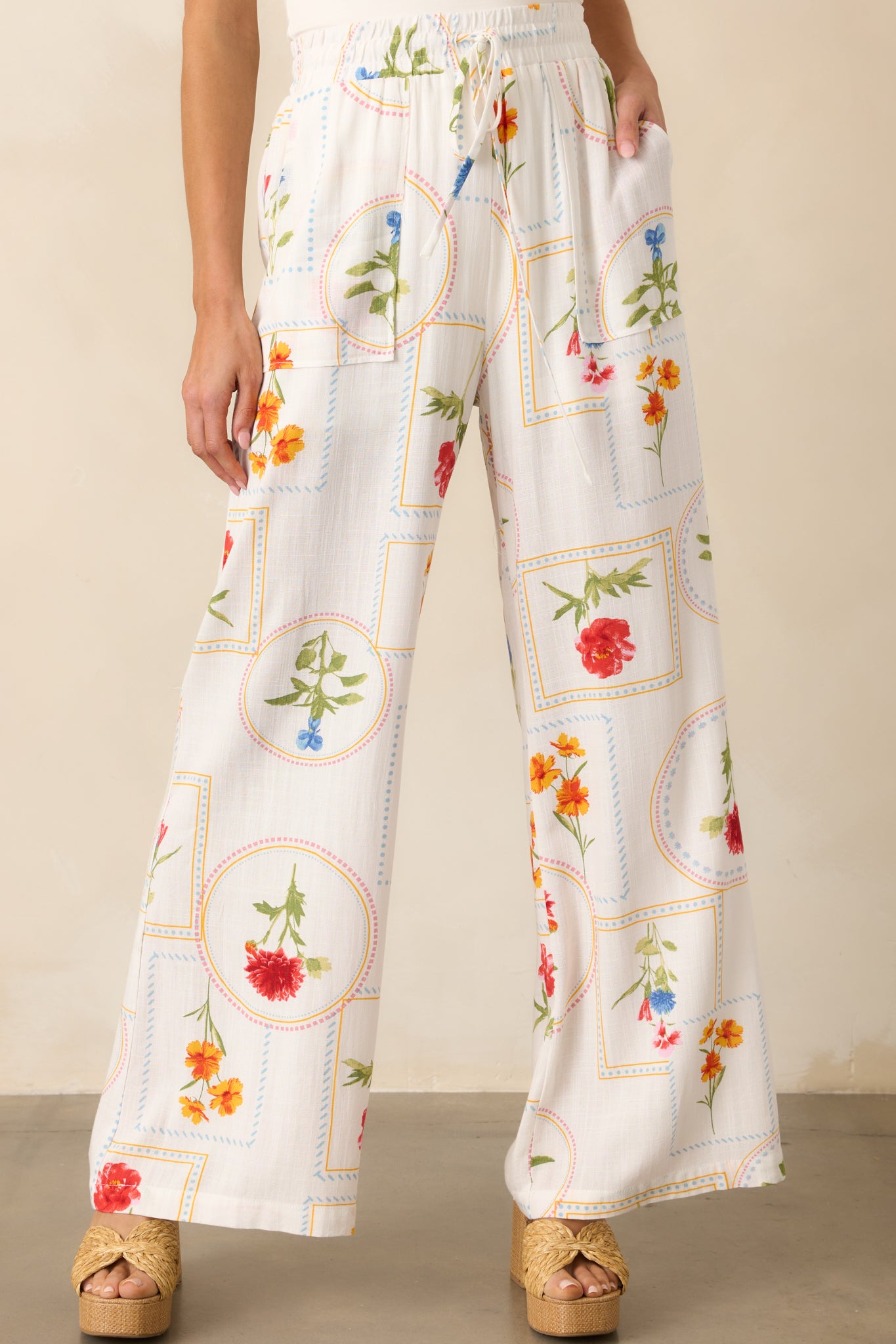 A detailed view of the functional patch pocket and intricate floral patchwork design on the ivory wide-leg pants.