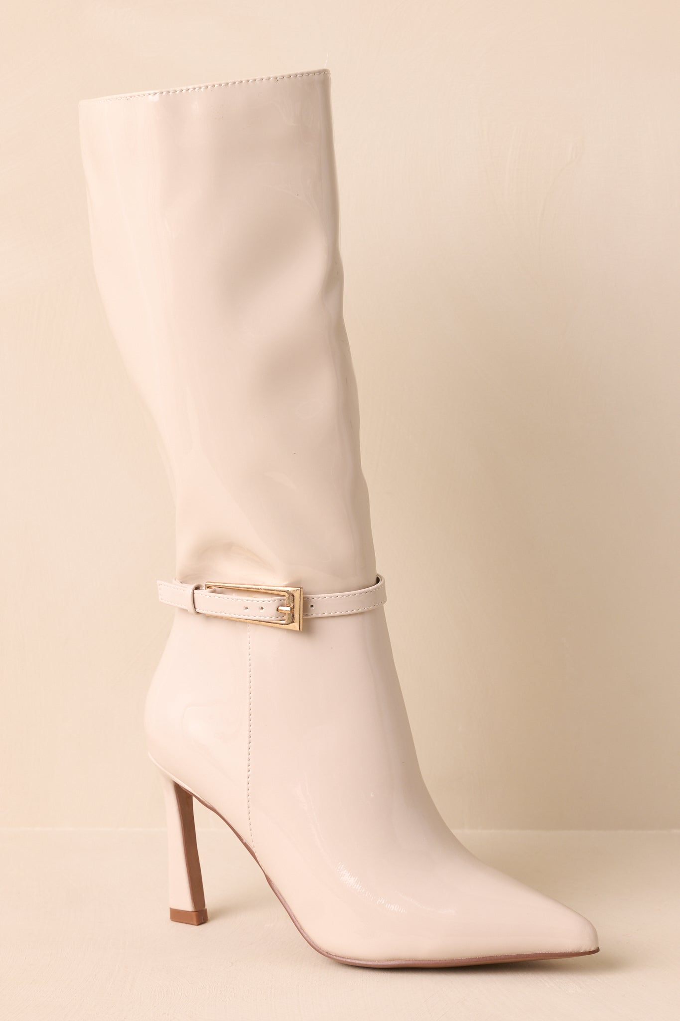 Ivory patent faux leather boots displaying their pointed toes and slim stiletto heels in a clean ivory sheen.
