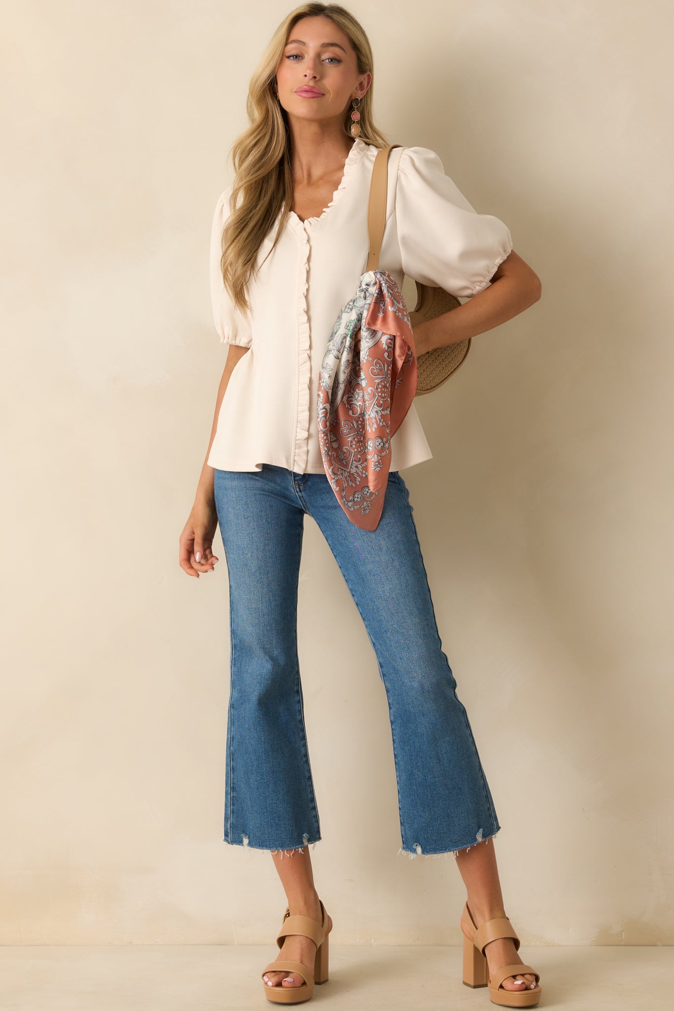 Front view of ivory peplum top featuring elastic-cuffed puff sleeves, ruffled V-neckline, and decorative button placket.