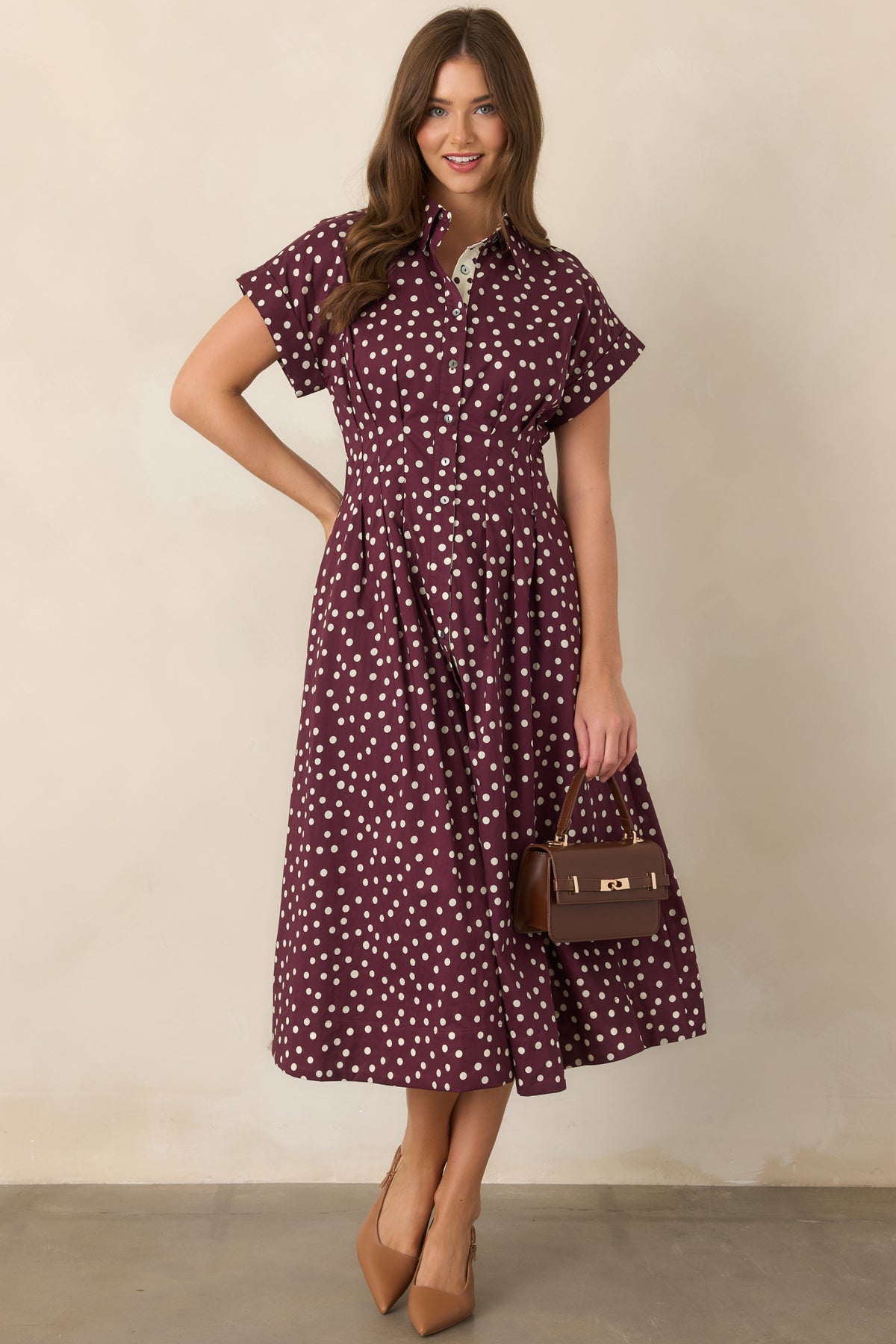Ivory and plum polka dot cotton midi dress with a collared neckline, button-front closure, short sleeves, tailored waist seams, and flowing fit-and-flare skirt with side pockets.