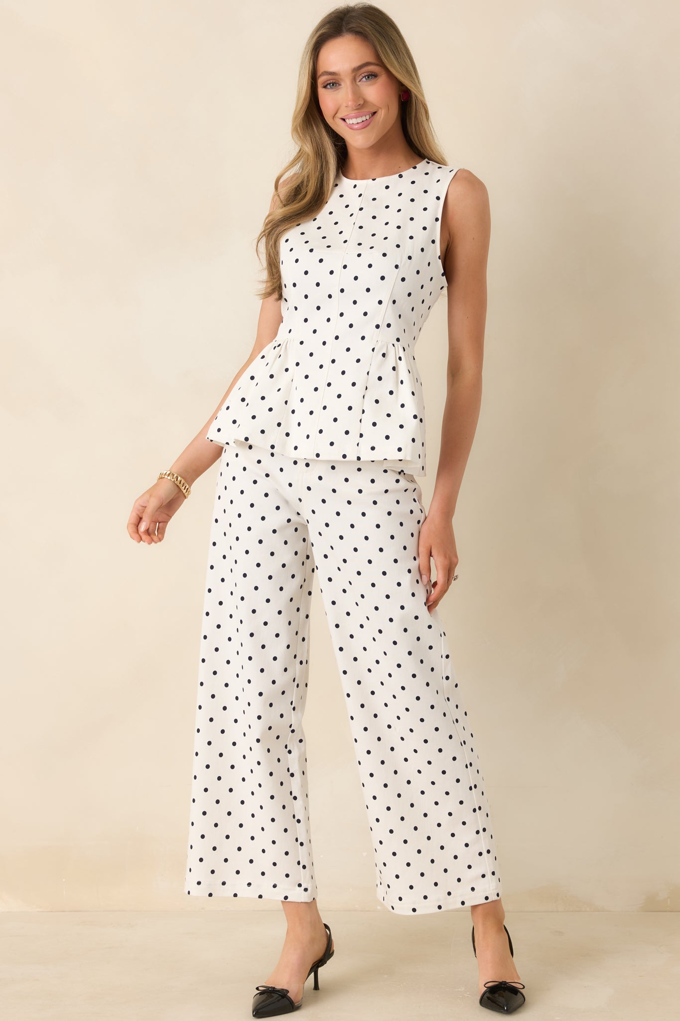 Ivory polka dot peplum top with sleeveless design, structured bodice, and flared waist.
