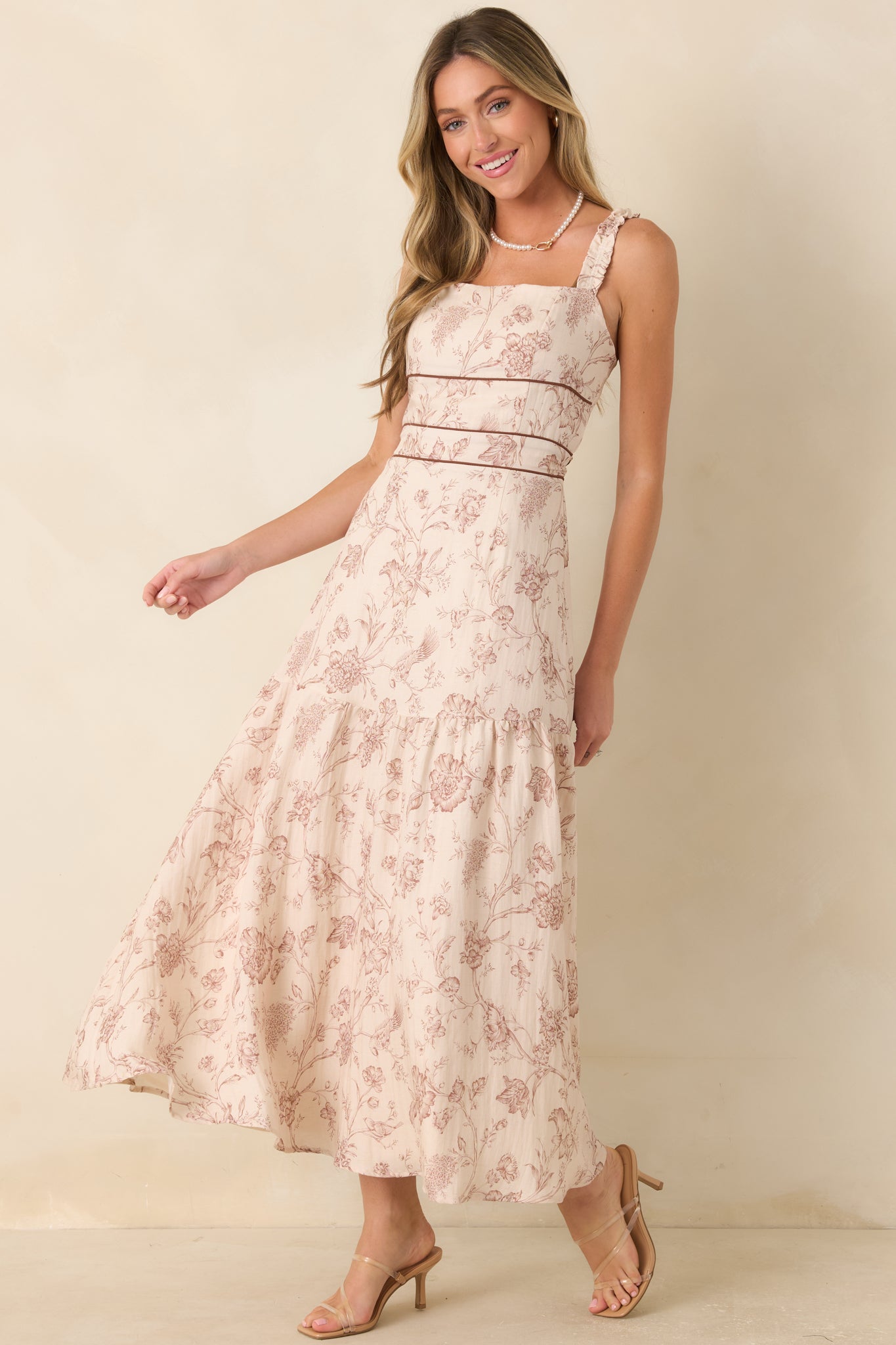 Ivory printed maxi dress showcasing contrast piping details, ruffled shoulder straps, and a graceful tiered skirt silhouette.
