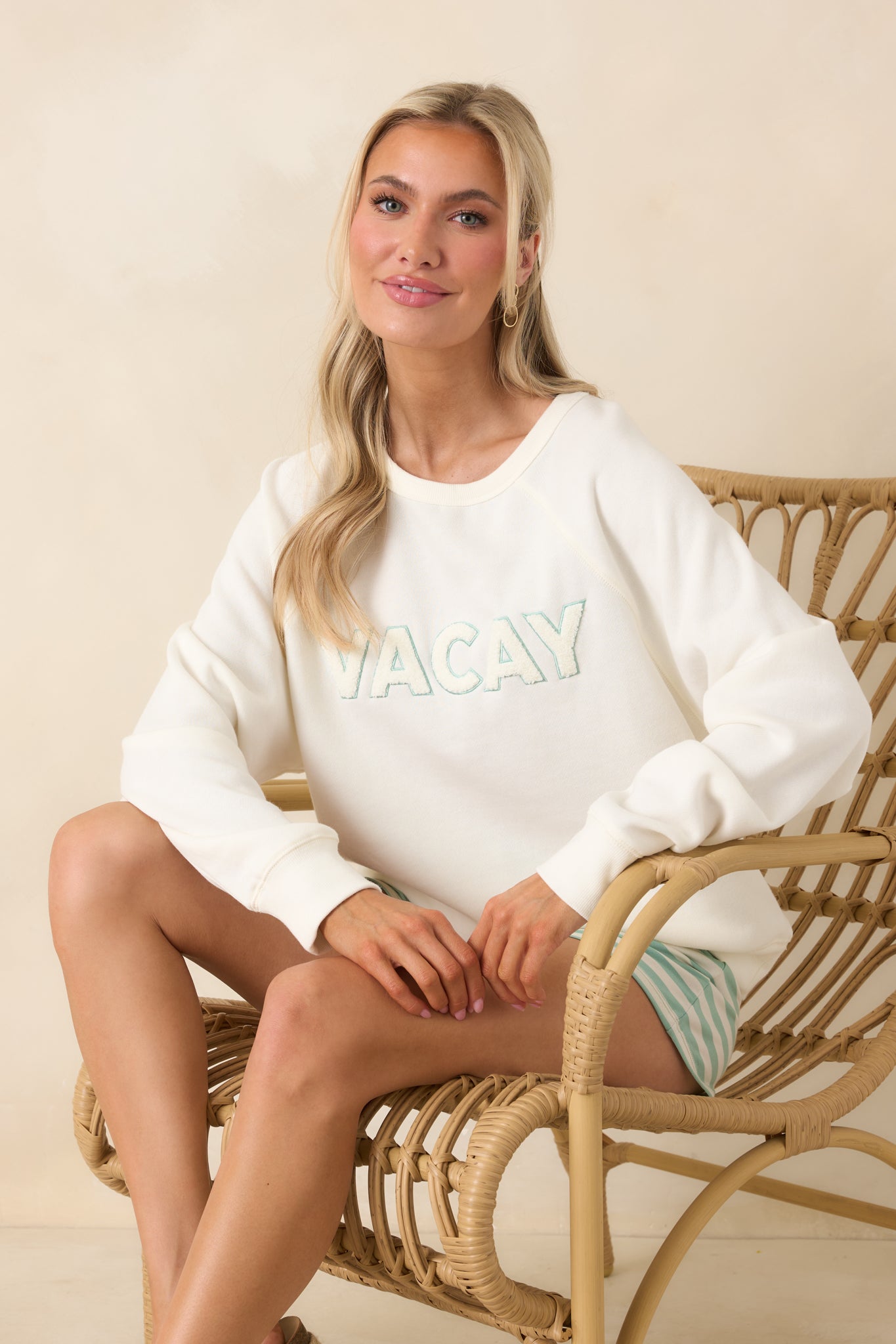 Neutral ivory pullover designed with a crew neck, breathable knit feel, and raised applique “VACAY” detail across the front.