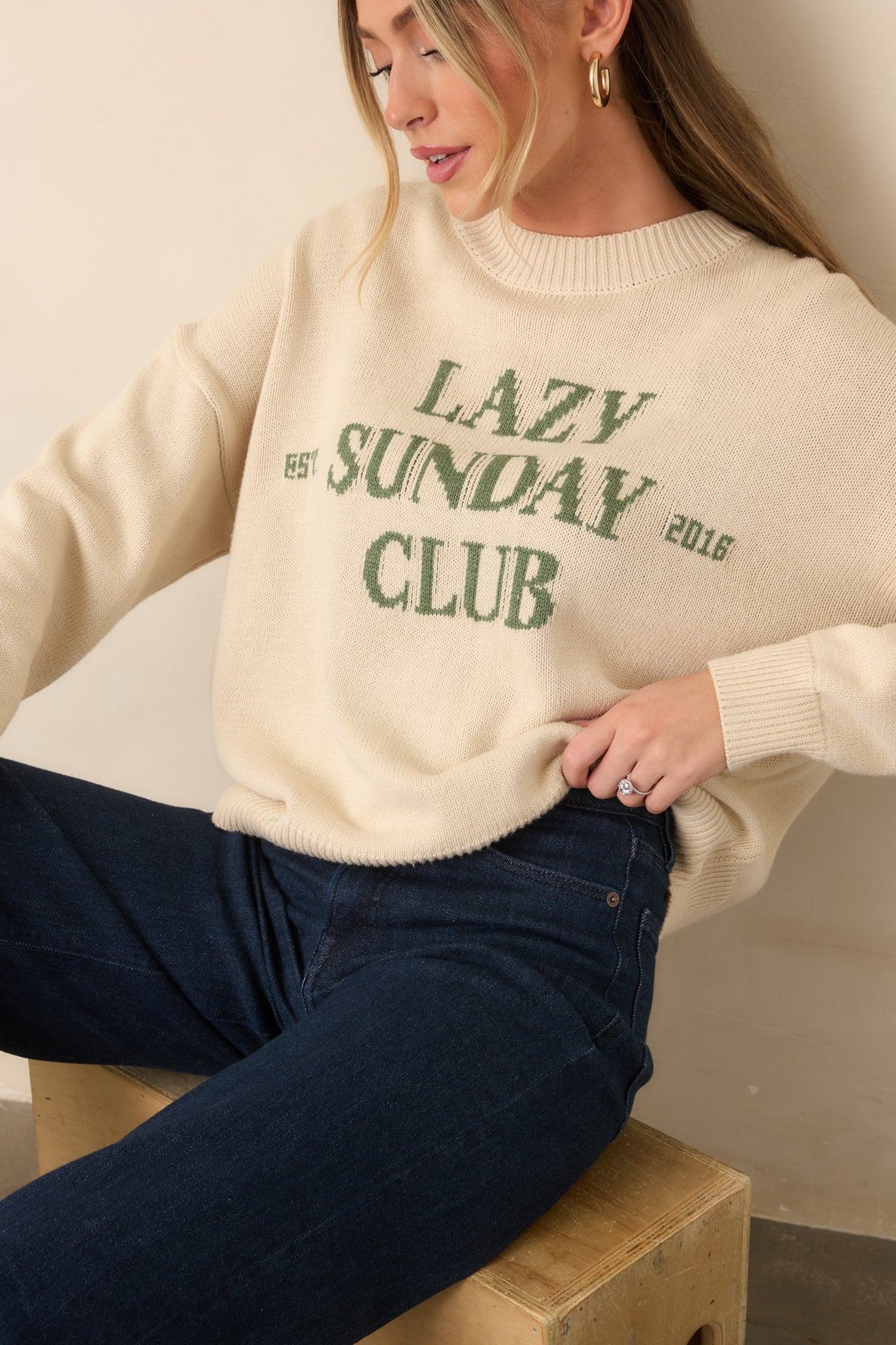 Ivory pullover sweater showcasing the green knit lettering, soft texture, and ribbed sleeve cuff.