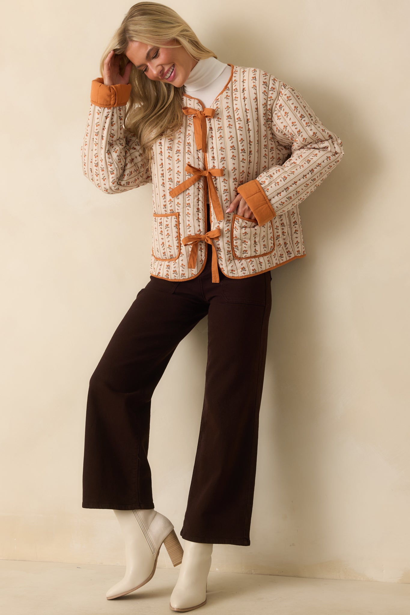 A full front view of the ivory quilted jacket with orange floral print, contrast orange trim, and self-tie bow closures.