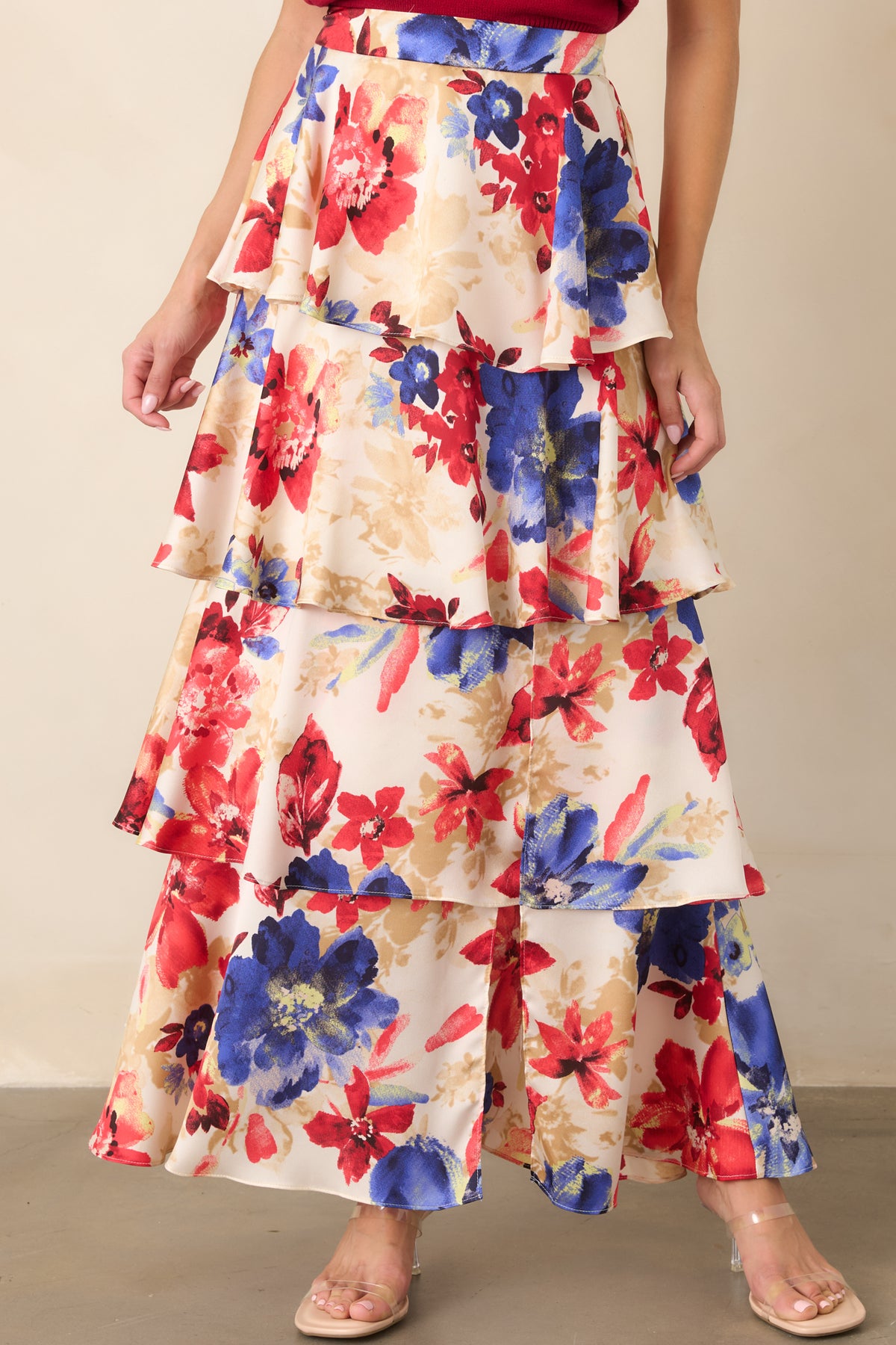 Close view of the layered skirt showcasing the flowing tiers and bold red floral motifs across the ivory fabric.
