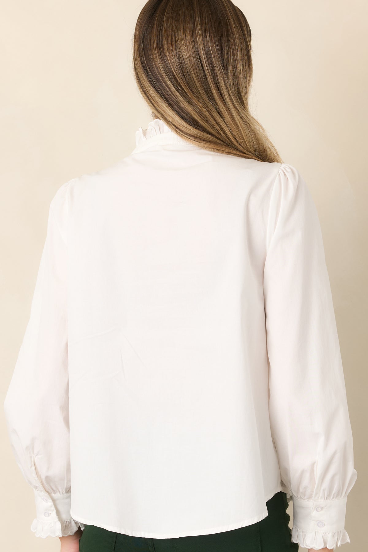 Rear view of the ivory blouse showcasing its relaxed silhouette, ruffle-trimmed shoulders, long sleeves, and softly gathered cuffs.