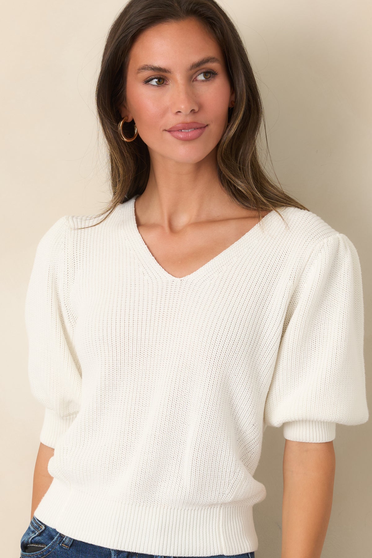 Ivory top showcasing the ribbed hem and wide cuffs against its smooth knit construction.
