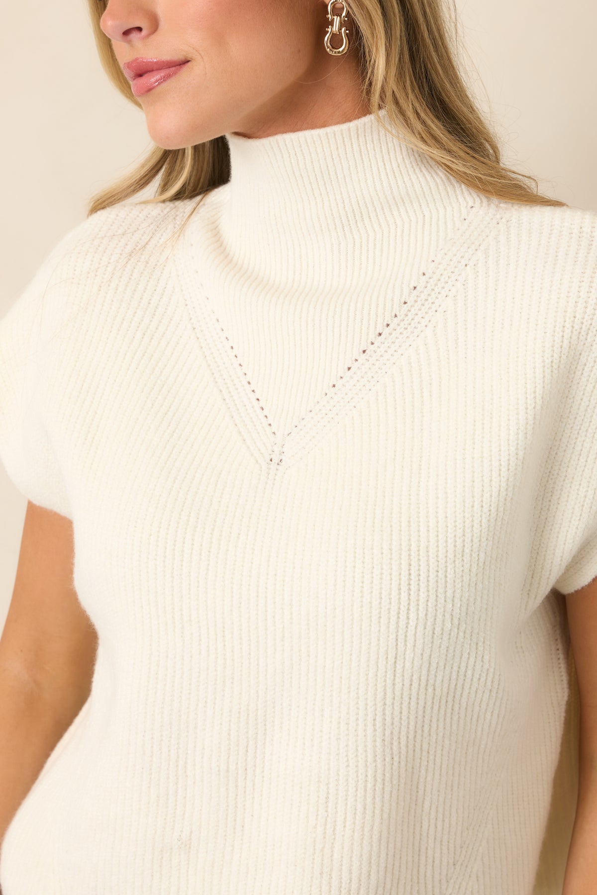 Close-up highlights the ribbed knit texture, mock neckline, cap sleeve construction, and subtle chest detailing.