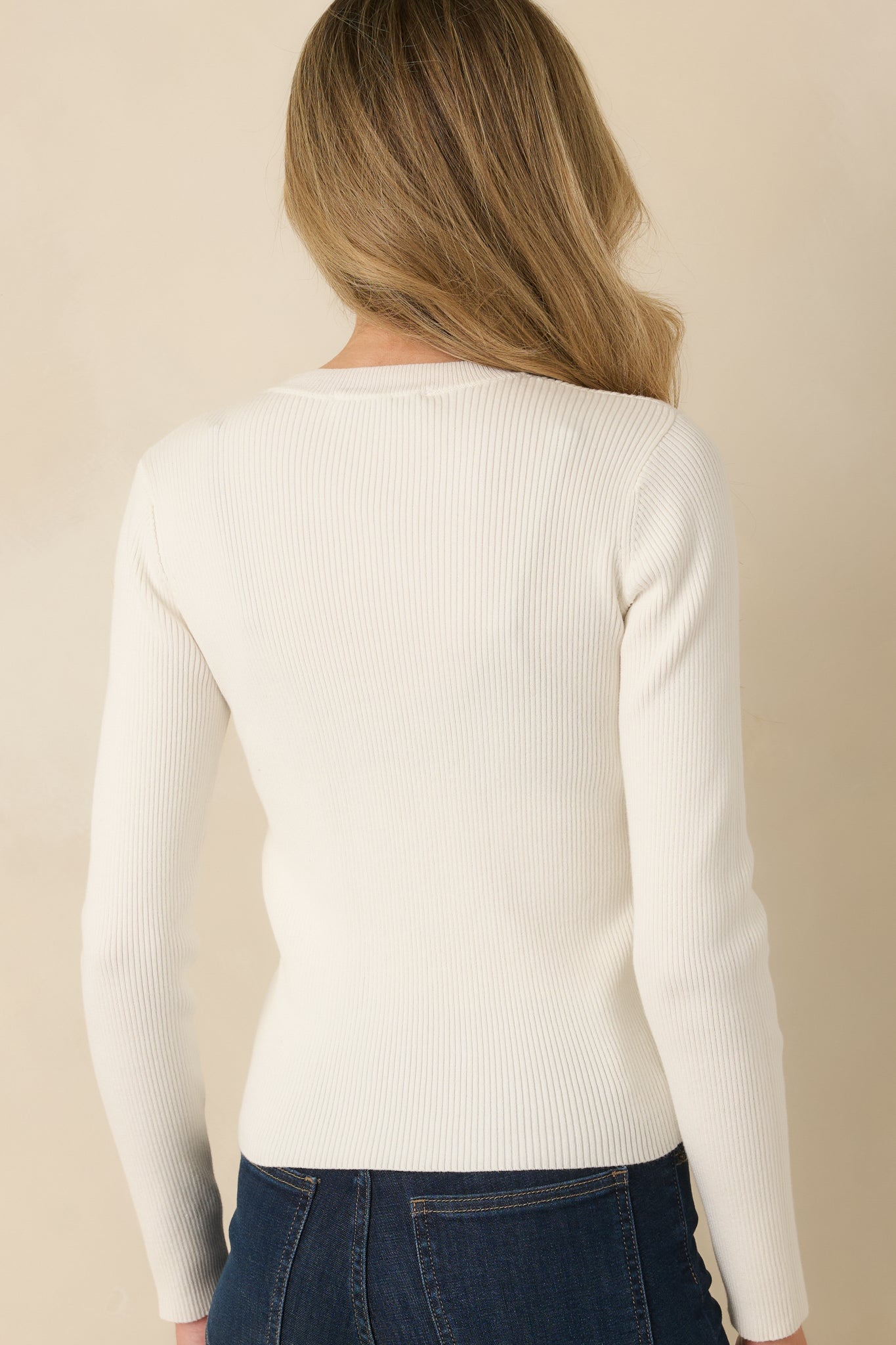 Back view of ivory ribbed knit top showcasing the fitted silhouette, crew neckline, and sleek long sleeves.