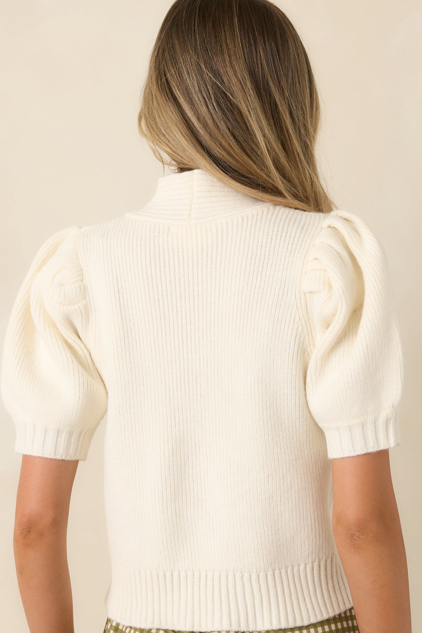Rear view of the ivory ribbed knit top featuring puff sleeves, a fitted silhouette, and a structured ribbed hem.