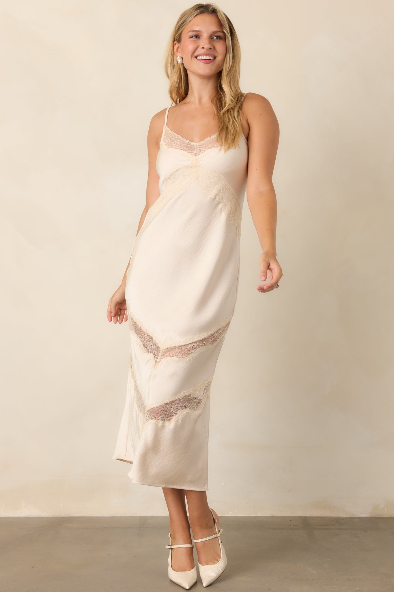 Ivory satin dress featuring slender adjustable straps, a lace-trimmed V-neckline, and a fluid body-skimming silhouette.