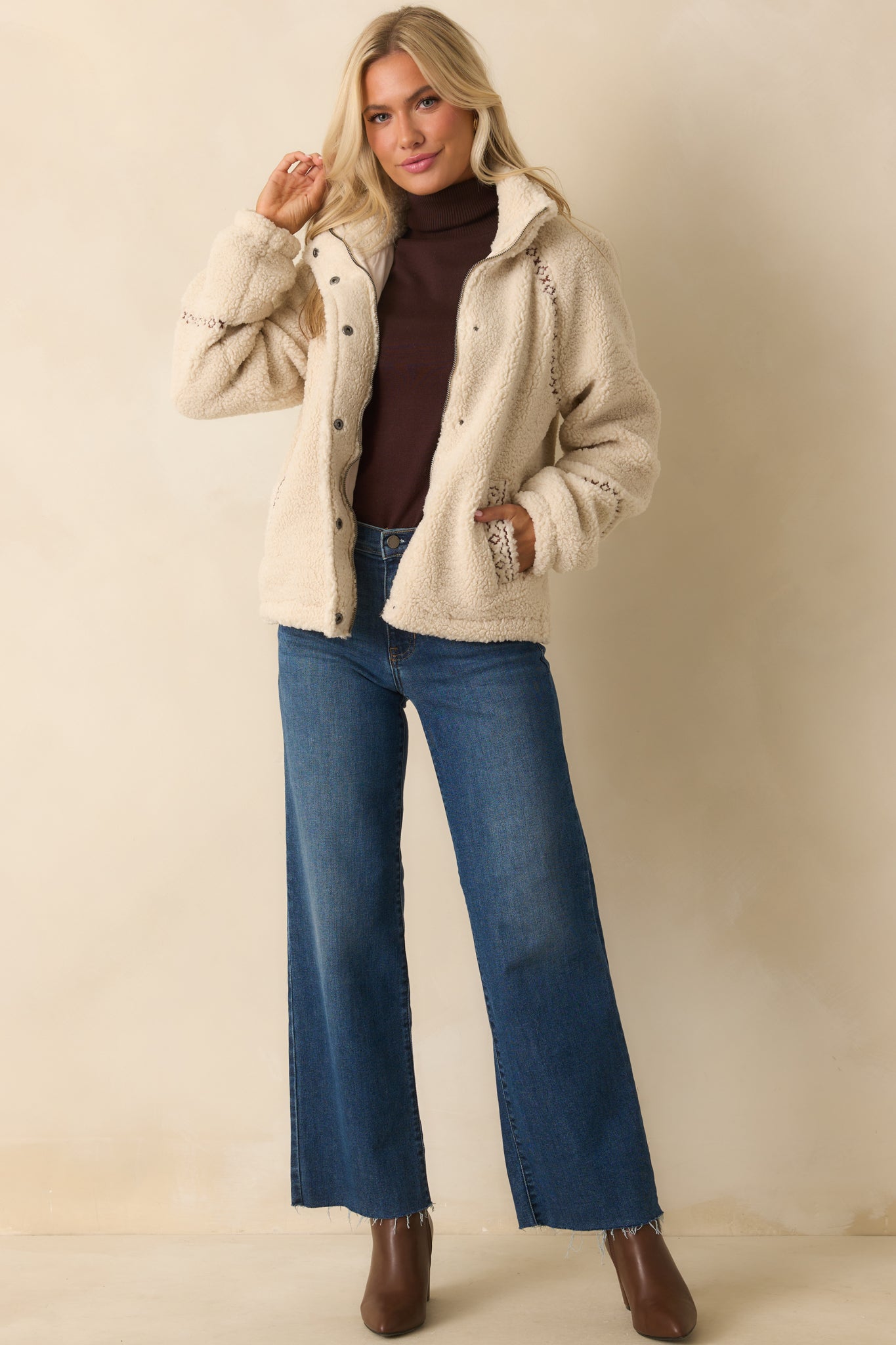 Ivory sherpa jacket with stand collar, full zip and snap button front, long sleeves, and embroidered contrast trim.