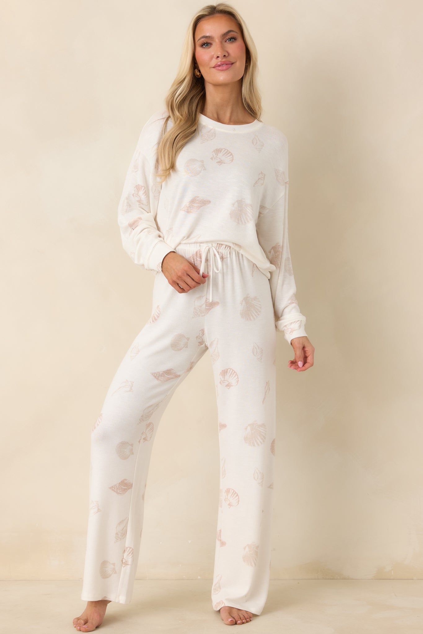 Ivory pajama pants with neutral seashell print, elastic waistband, adjustable drawstring tie, and relaxed wide-leg silhouette.