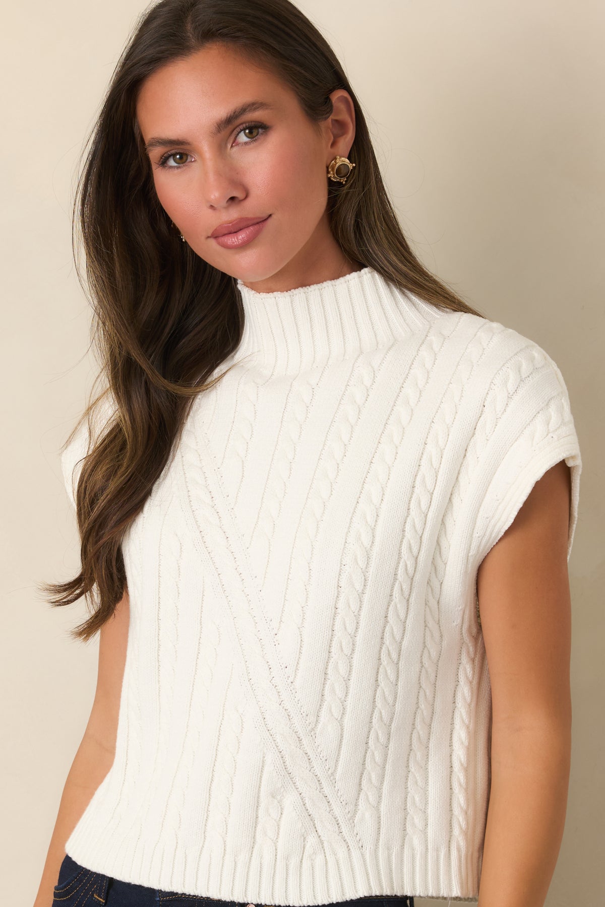 Sleeveless ivory cable-knit top combines a polished mock neck with a relaxed shape designed for layering.