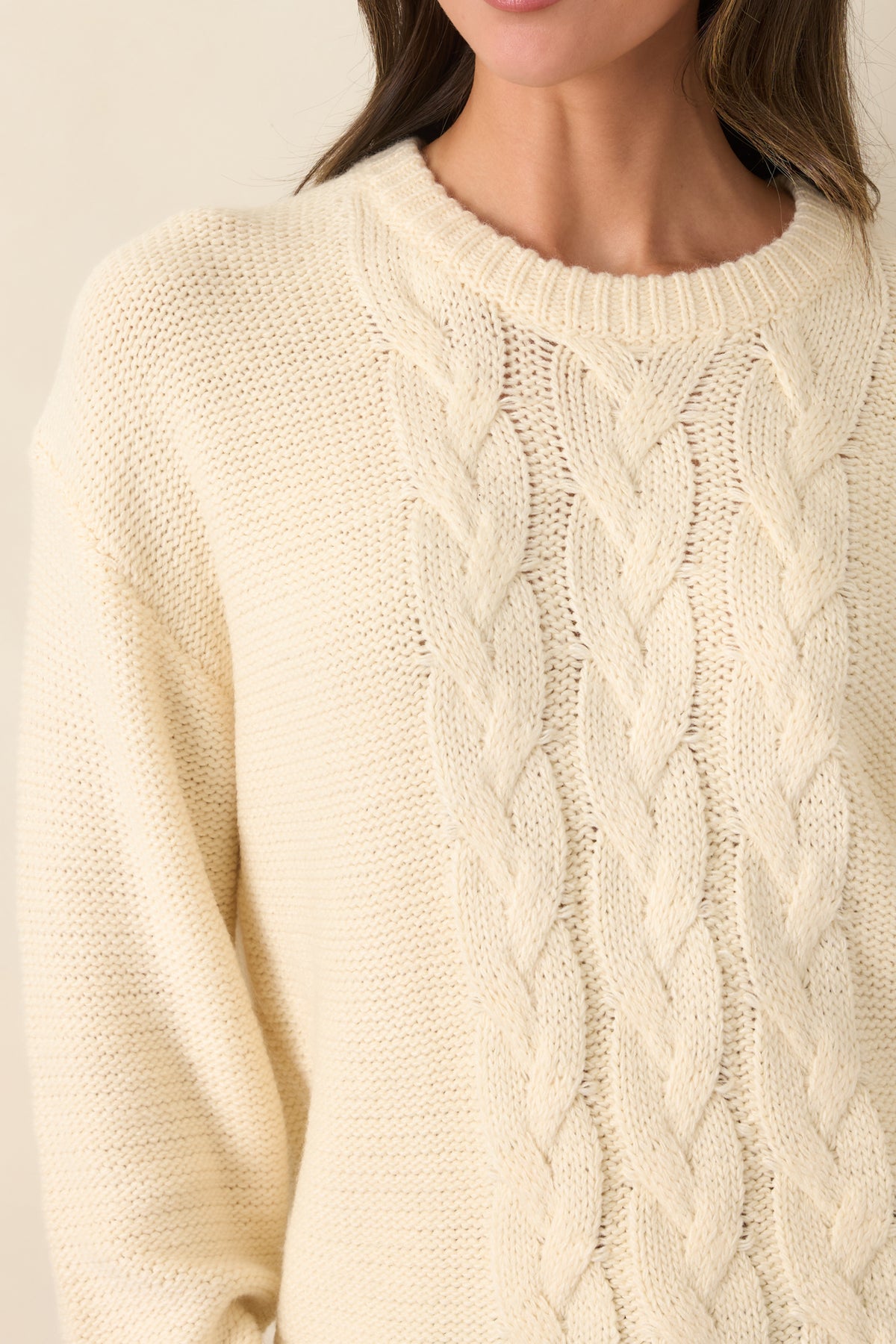 Close-up detail of the ivory sweater showing its textured cable knit design and soft knit construction.