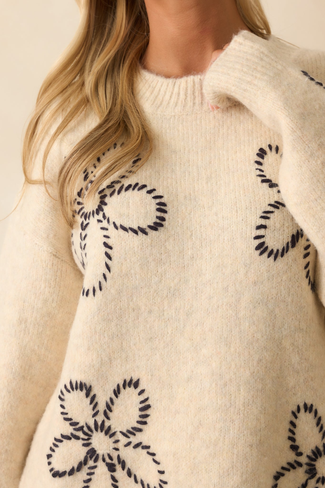 Zoomed-in view of the black embroidered floral stitches and ribbed hem texture on the ivory sweater.