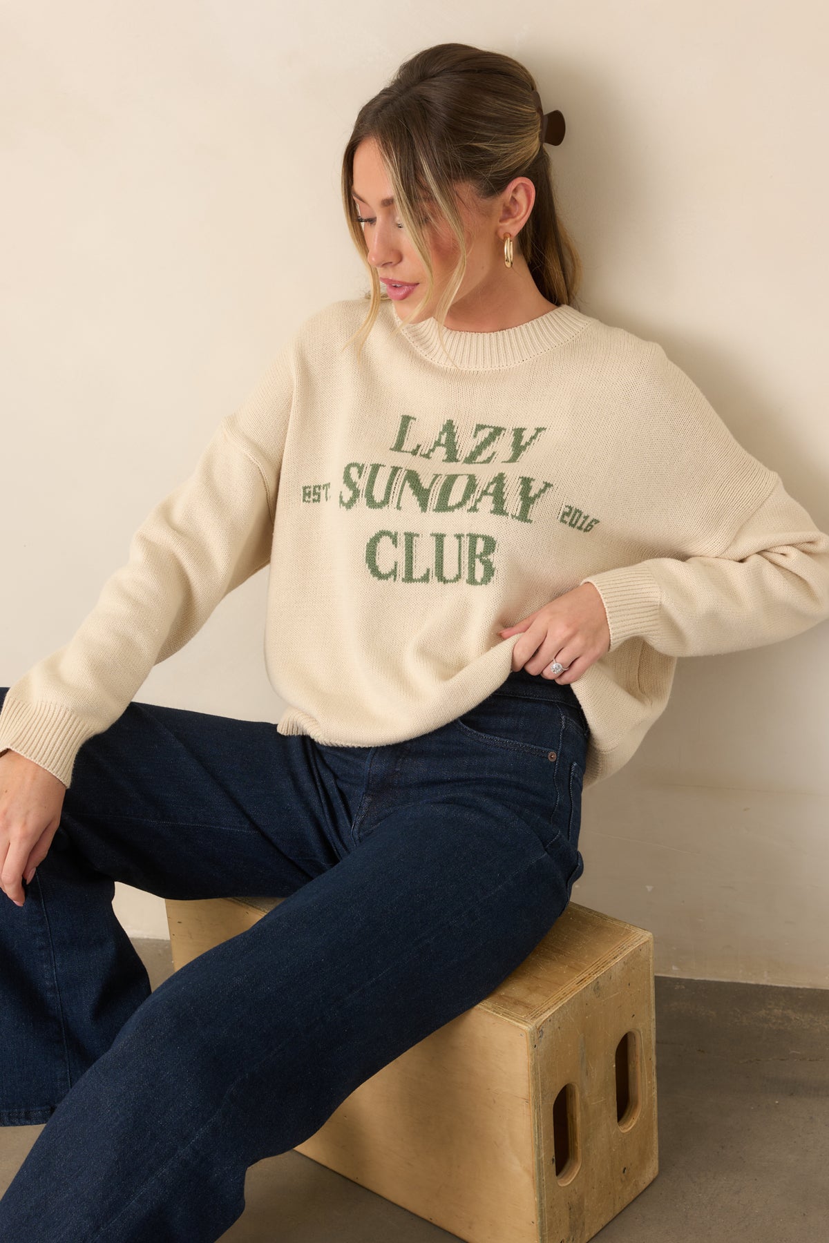 Ivory knit sweater highlighting the relaxed chest area, green graphic lettering, and ribbed neckline detail.