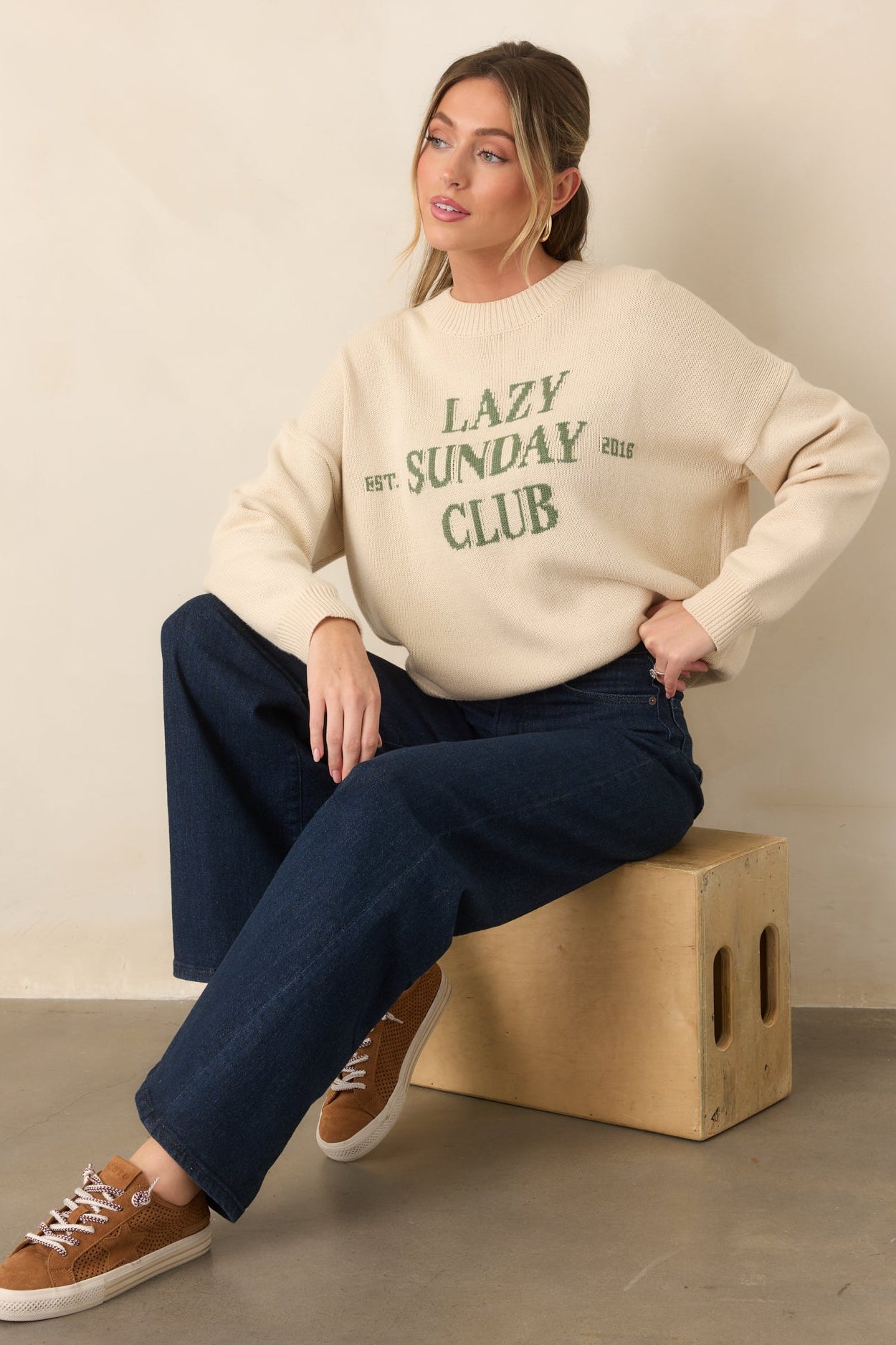 Green knit lettering stands out against the ivory sweater, complemented by a softly textured crew neckline.