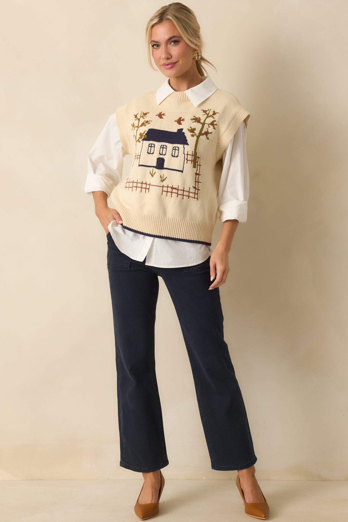 Ivory sleeveless sweater vest with a front intarsia house and tree motif and crew neckline.