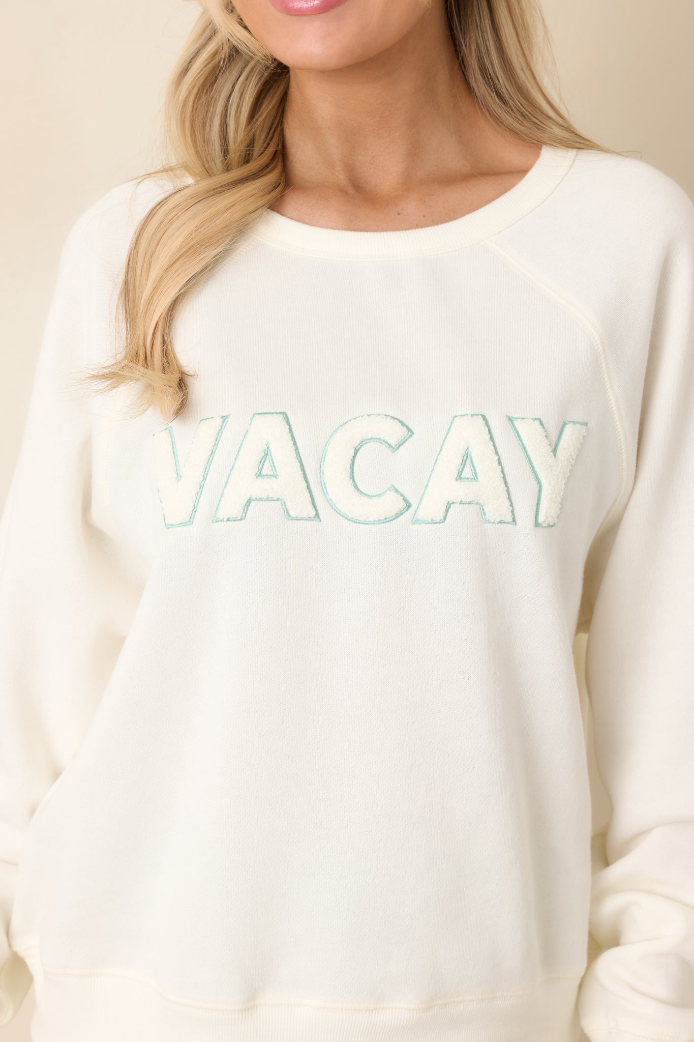 Close view of the raised “VACAY” applique showcasing textured stitching on the soft ivory fabric.