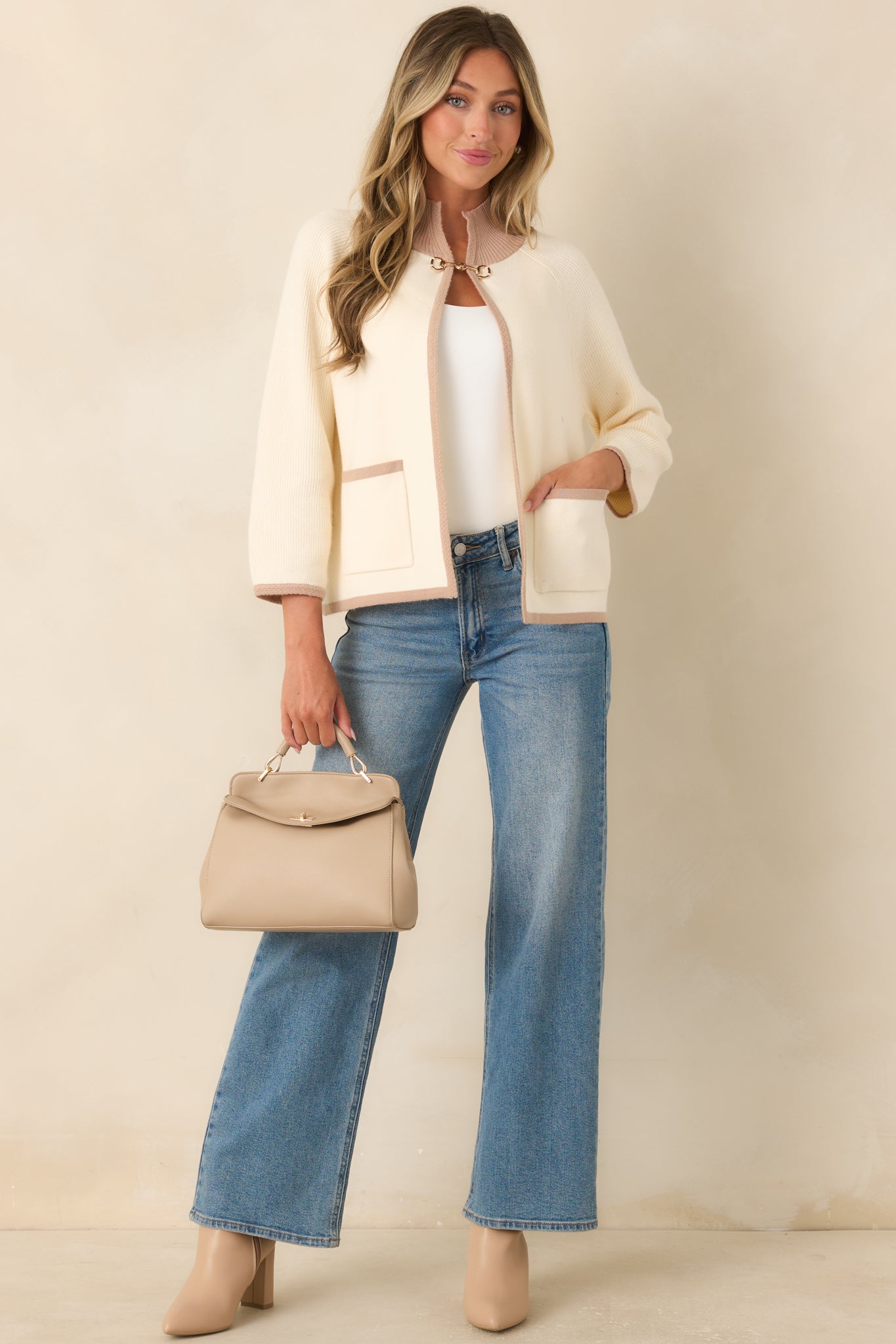Soft ivory knit cardigan featuring taupe contrast trim, ribbed edges, patch pockets, and a gold-tone horsebit closure on the open front.