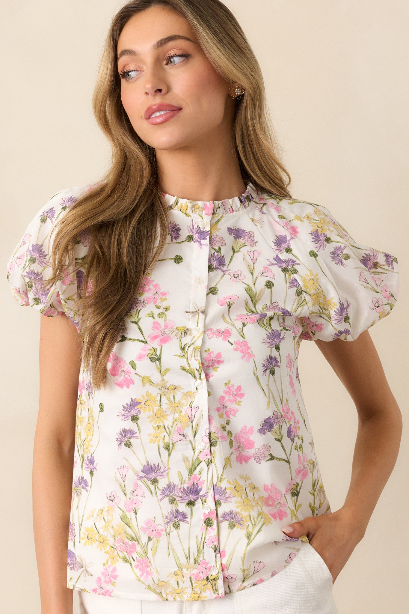 This ivory top features a pink multicolor floral print, with a functional button front and a ruffle trim neckline. Short puff sleeves with elastic cuffs complete the look, adding a touch of femininity to the design.