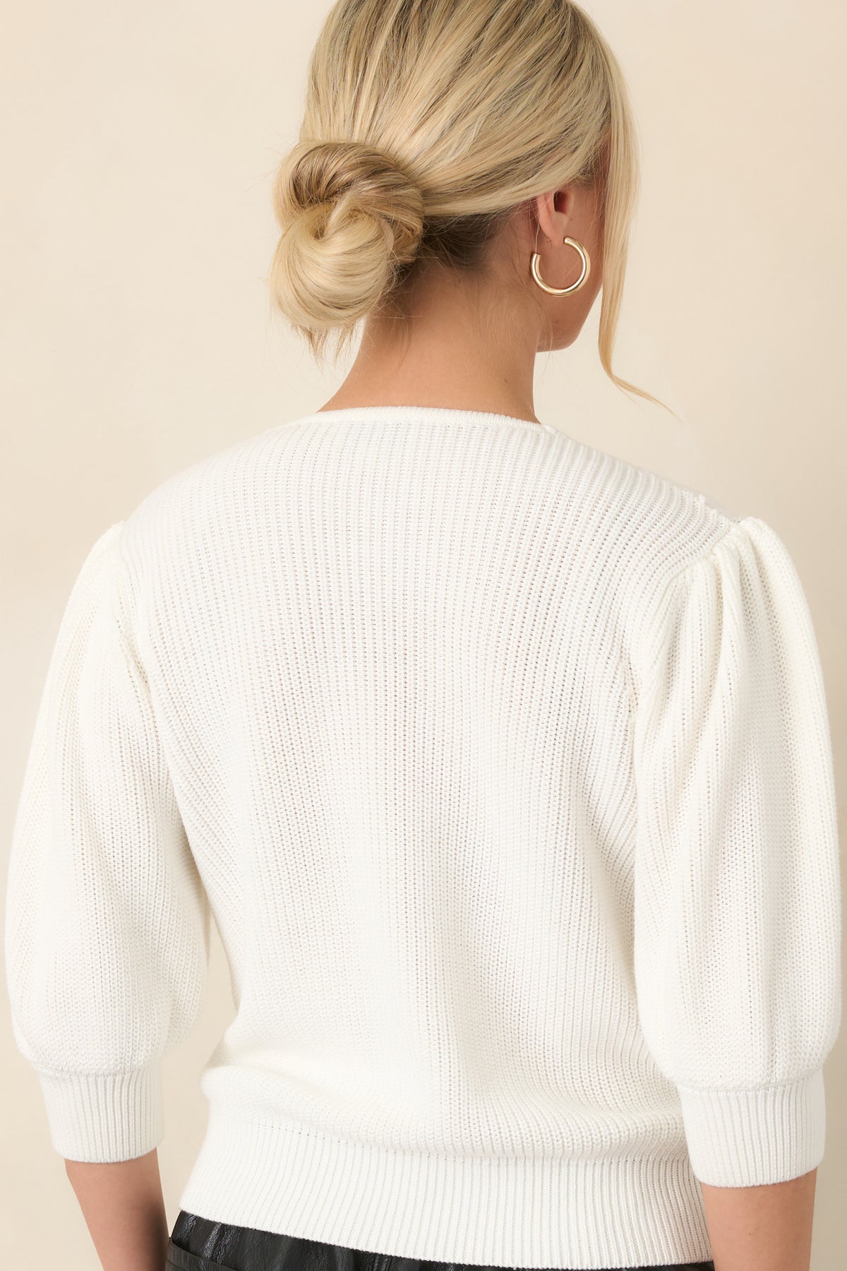 Rear view of the ivory top showcasing its softly structured silhouette, puff sleeves, and ribbed hem.