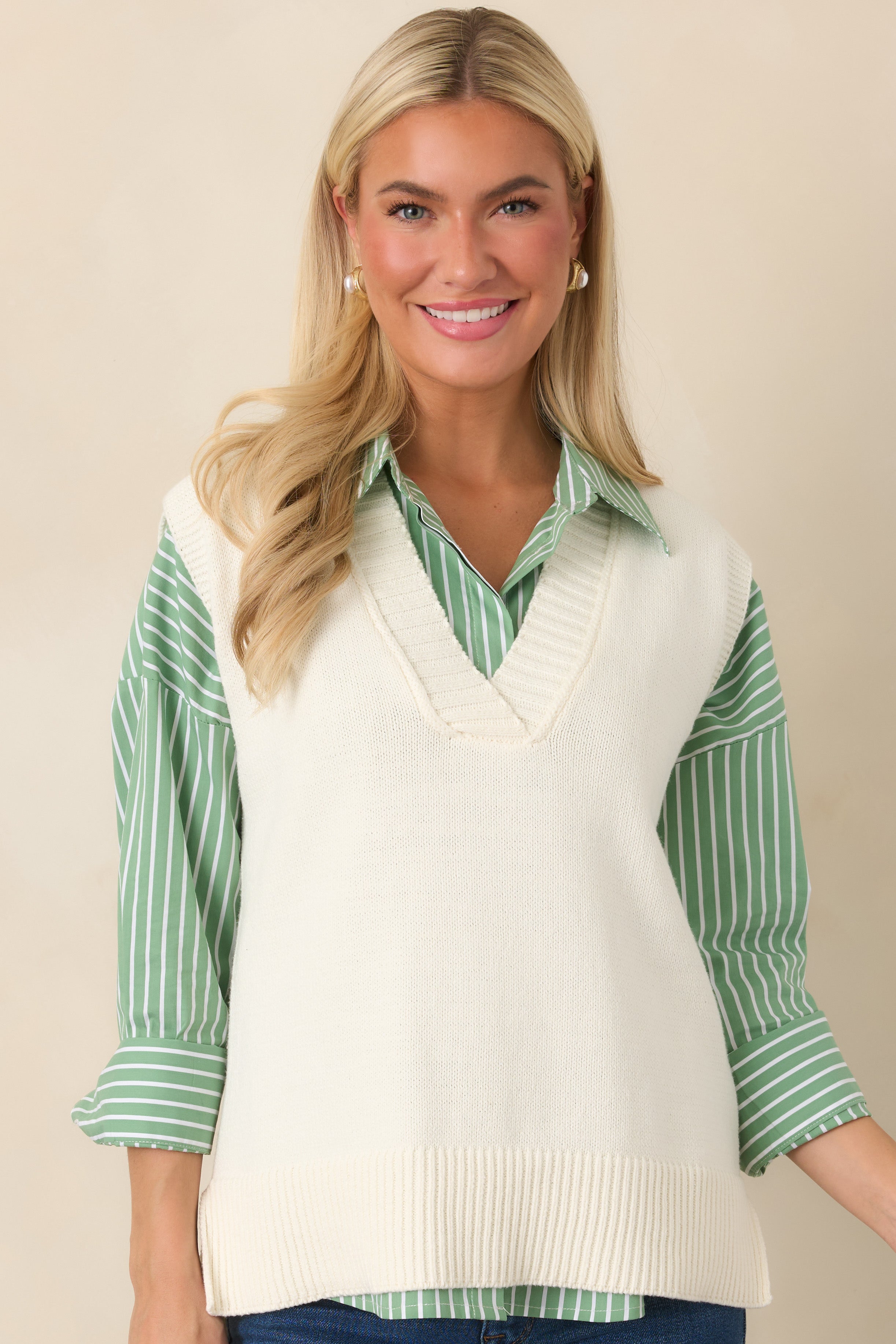 Detailed view of the ribbed V-neckline and arm openings against the soft ivory knit fabric.