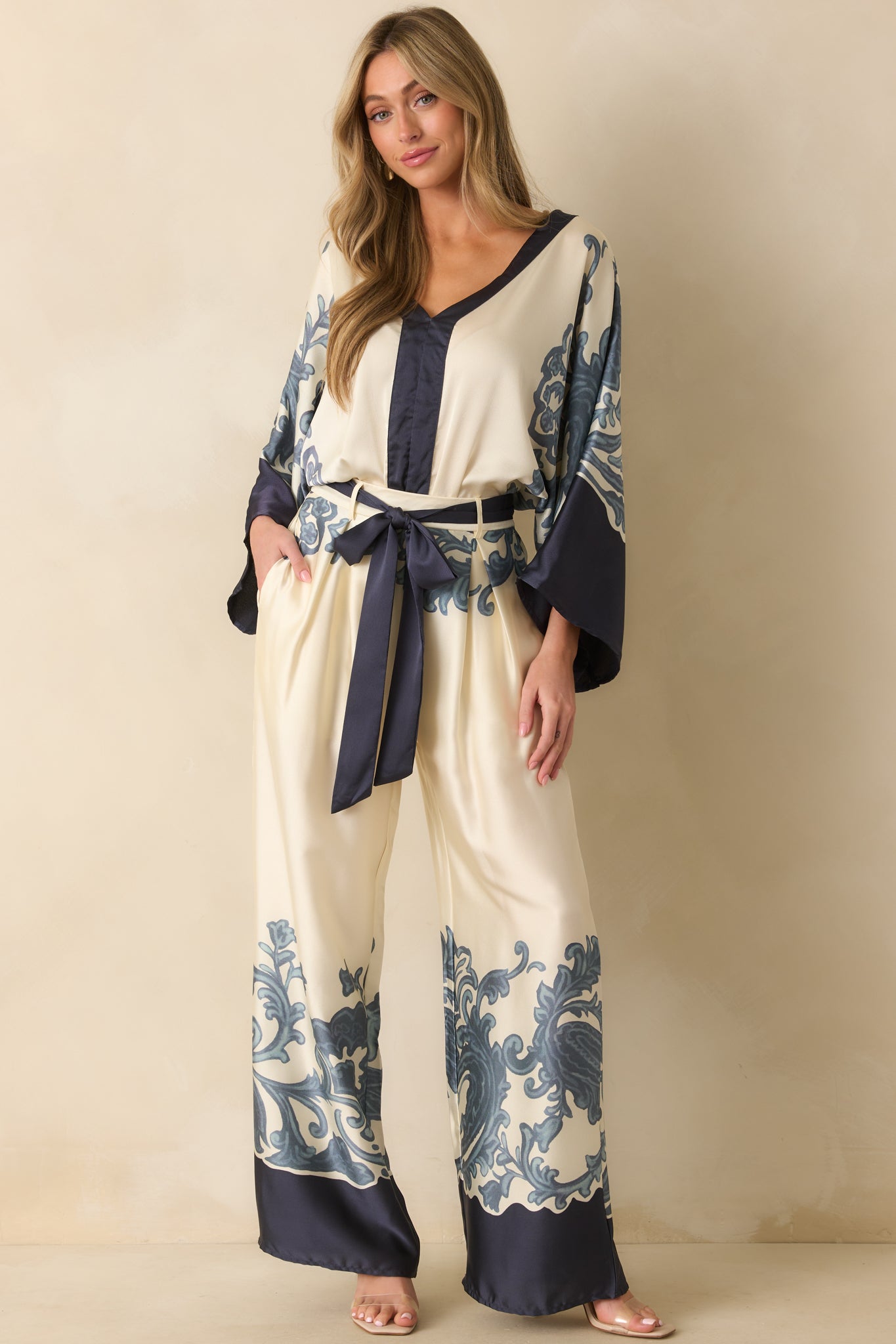 Front view of ivory wide-leg pants with navy baroque-inspired border print, showcasing the high-rise waist, optional sash belt, and functional pockets.