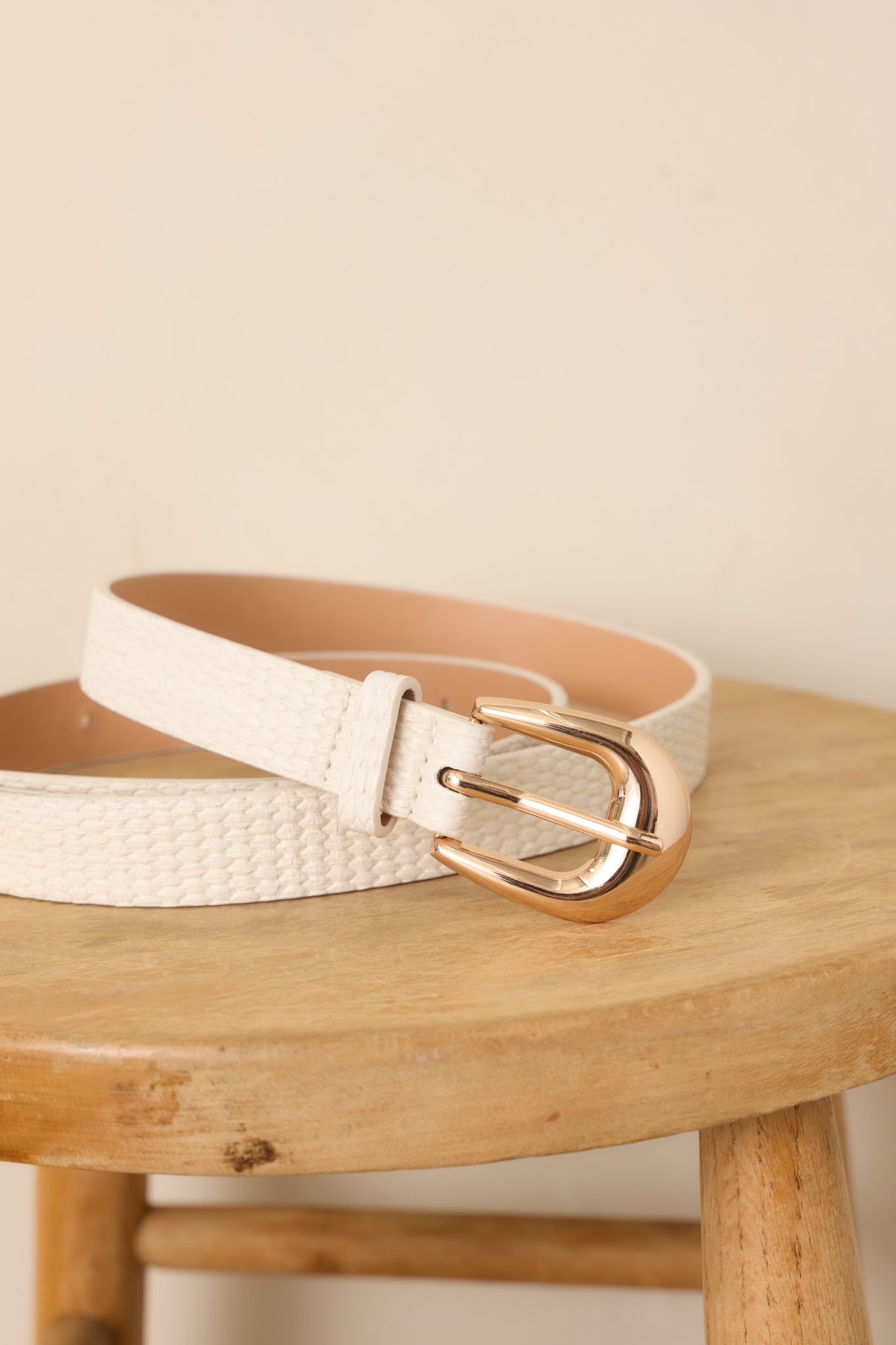 Close-up of the ivory belt highlighting the woven faux leather texture, gold-tone buckle, and neatly punched adjustment holes.