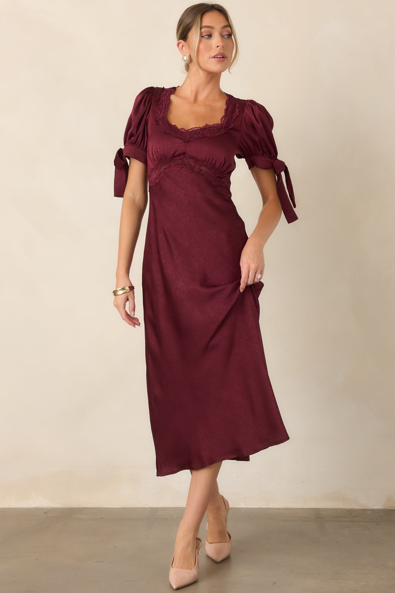 Jewel-tone satin midi dress featuring a lace-trimmed neckline, defined underbust seam, short puff sleeves, self-tie cuffs, and flattering empire waist.
