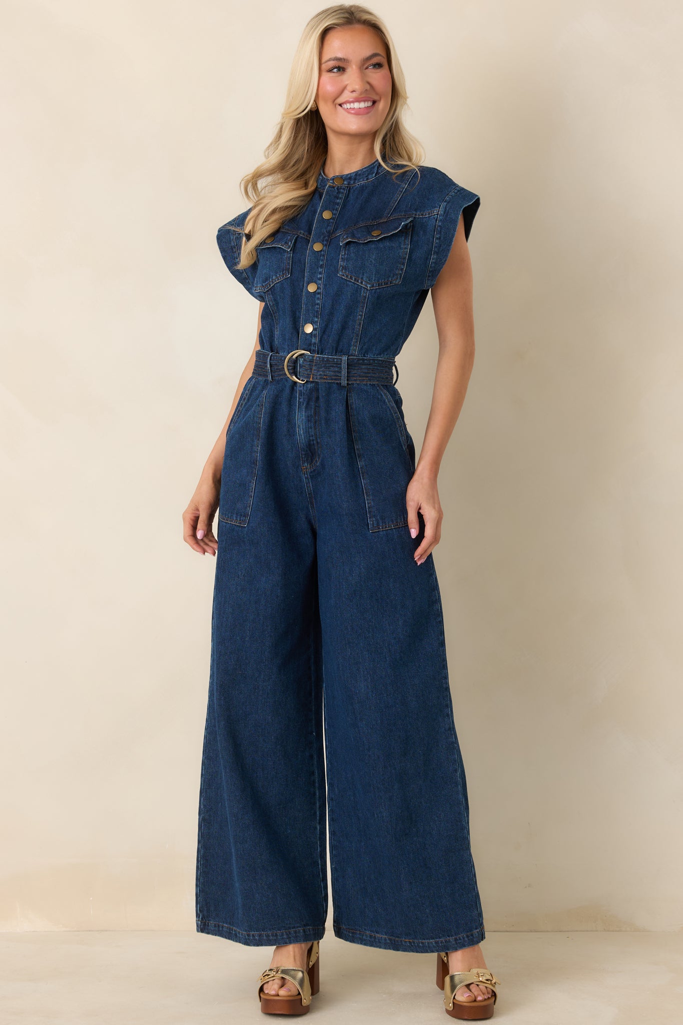Utility-style jumpsuit with snap-button front, cap sleeves, chest flap pockets, and wide-leg silhouette.